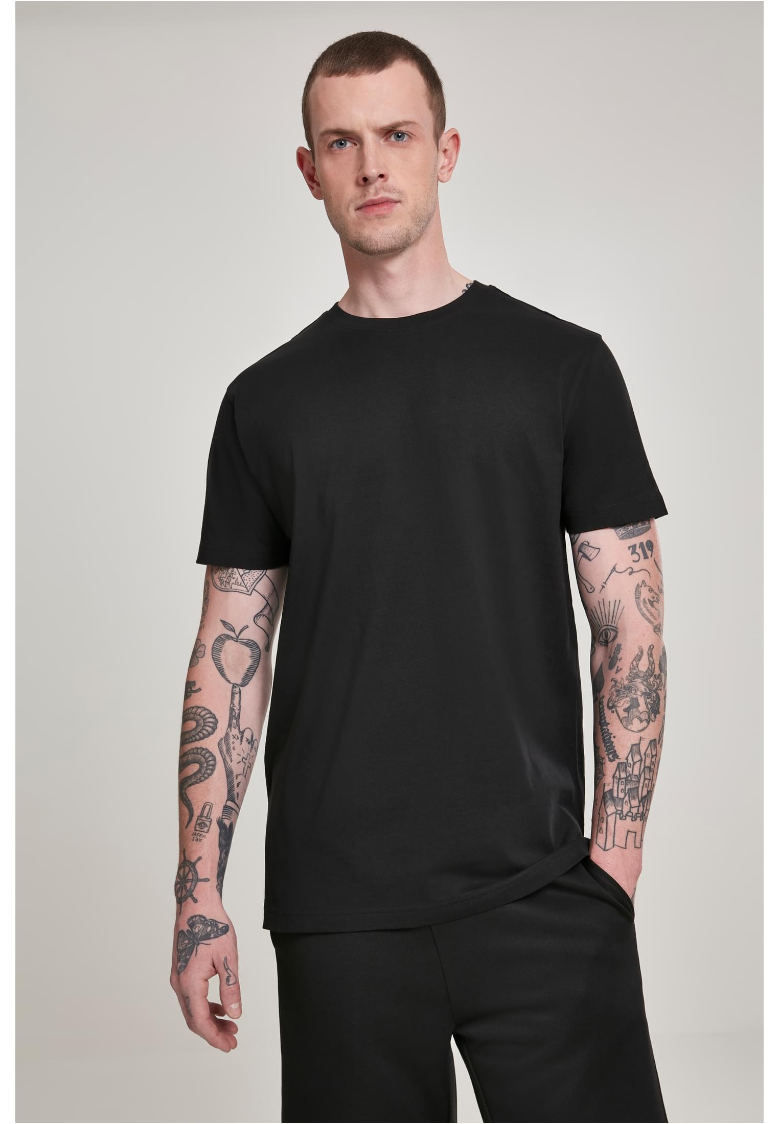 En man med tatuerade armar visar framsidan av en svart t-shirt.