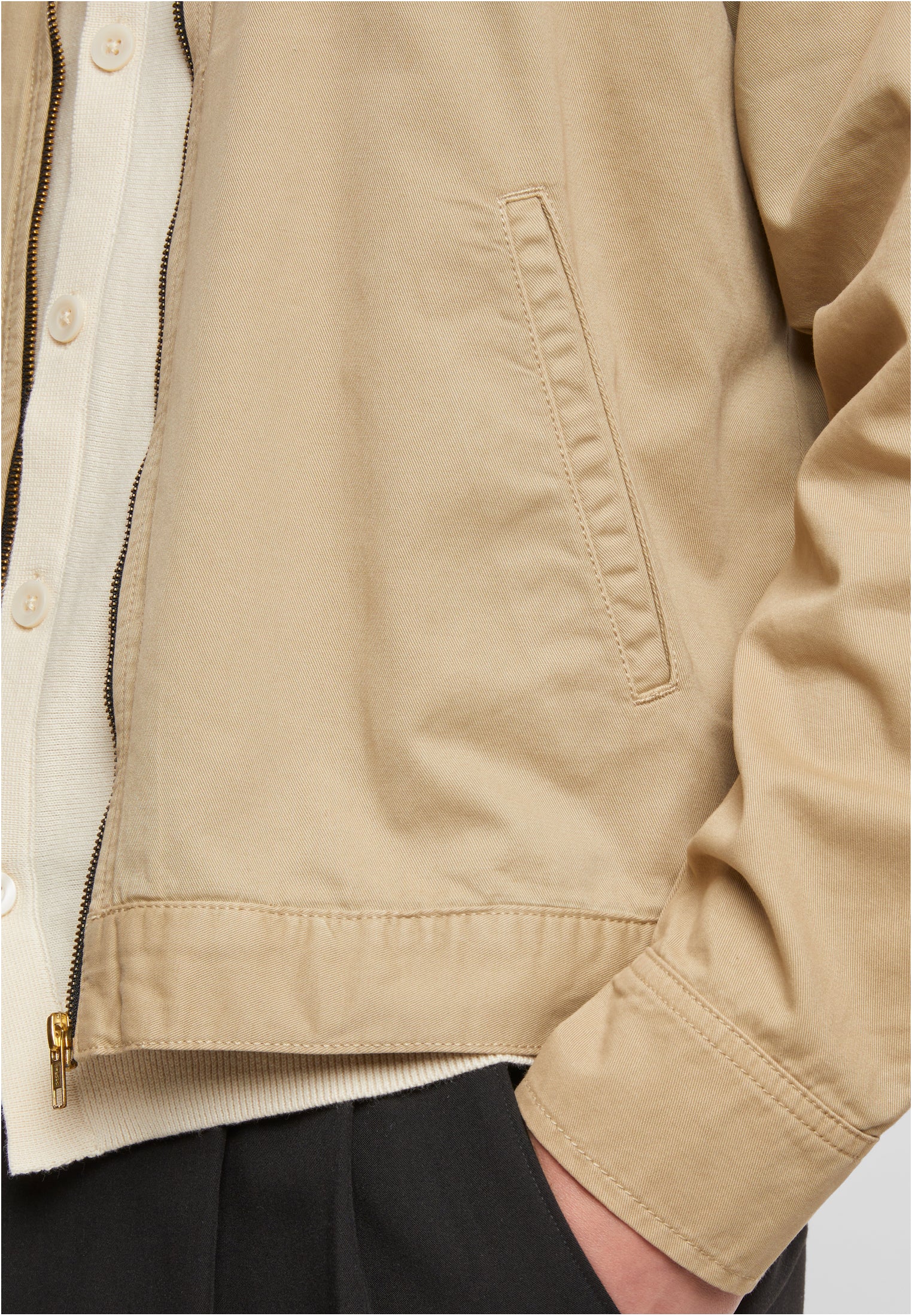 Närbild på en man som bär en beige UC Workwear Jacket, med fokus på den gyllene dragkedjan, sidfickan och tygets textur.