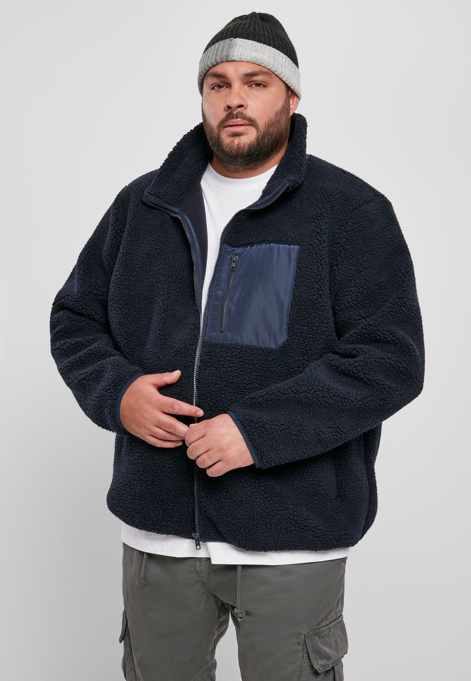 En man visar framsidan av den marinblå UC Sherpa Jacket mot en ljusgrå bakgrund.