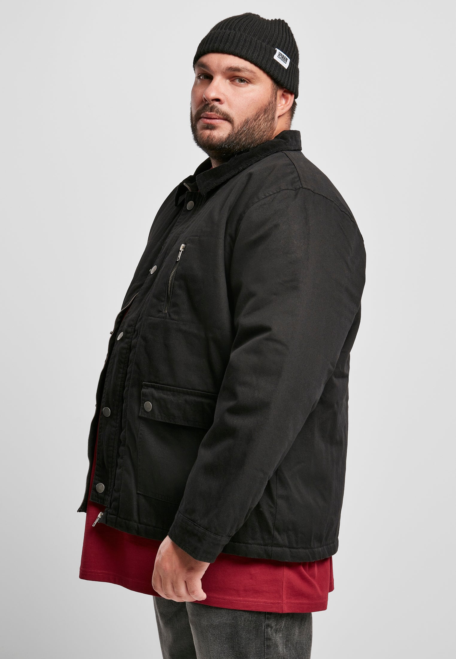 Sidoansikt av en man med skägg och mössa som bär en svart UC Hunter Jacket.