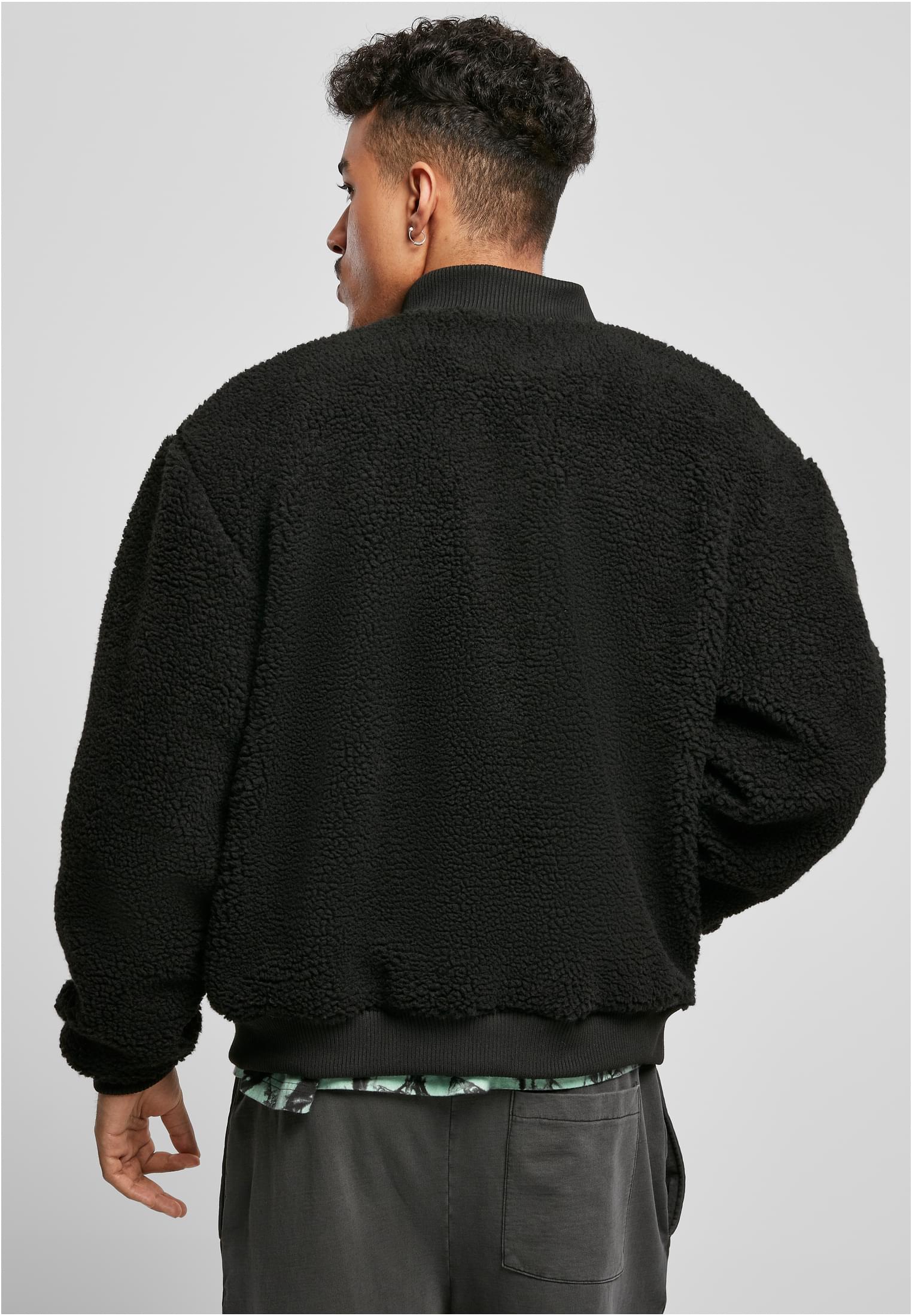 En man visar baksidan av en svart, fluffig sherpajacka med boxig passform.