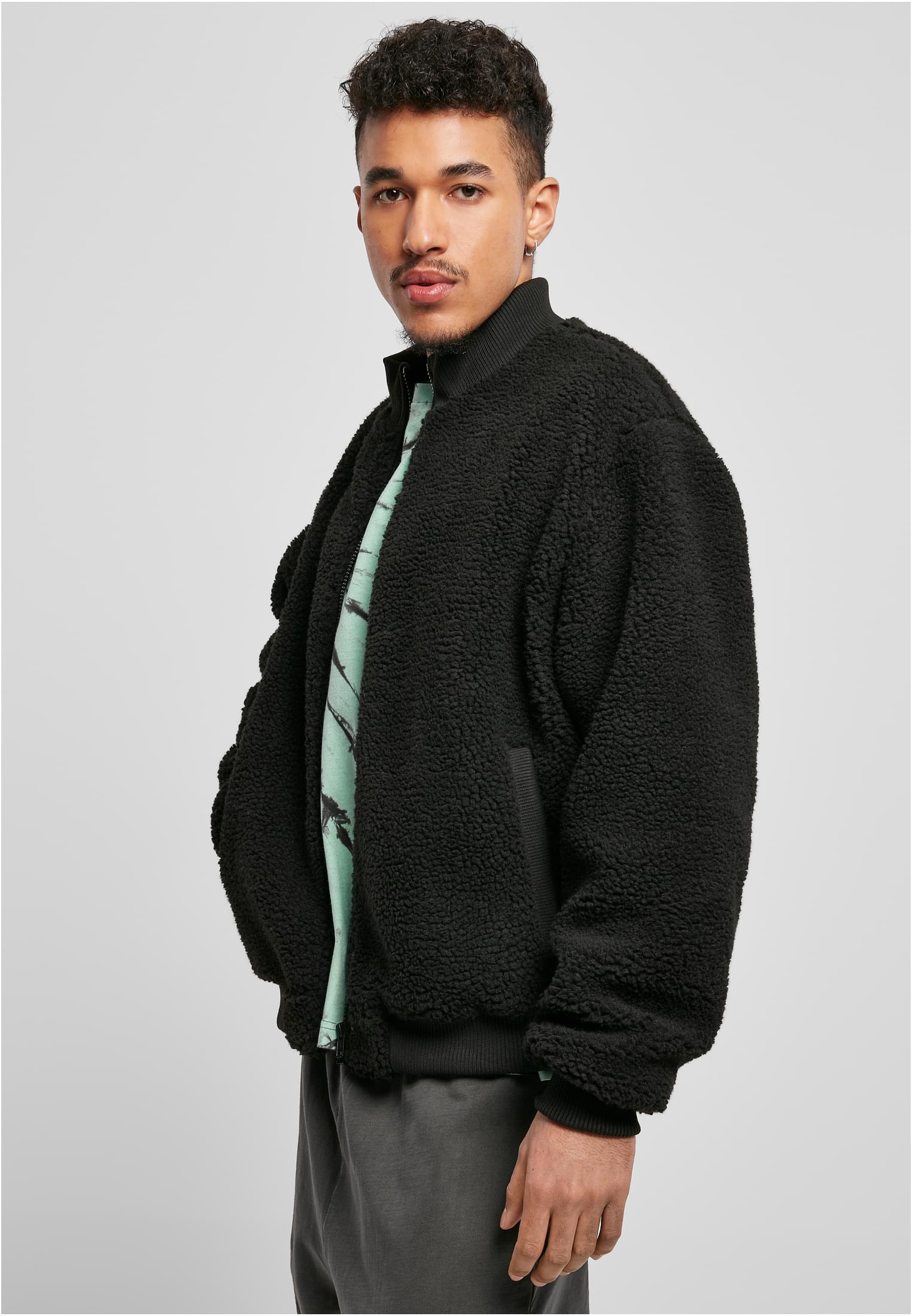 En manlig modell bär den svarta UC Boxy Sherpa Jacket. Jackan i fluffigt material bärs öppen och visar en mintgrön t-shirt under.