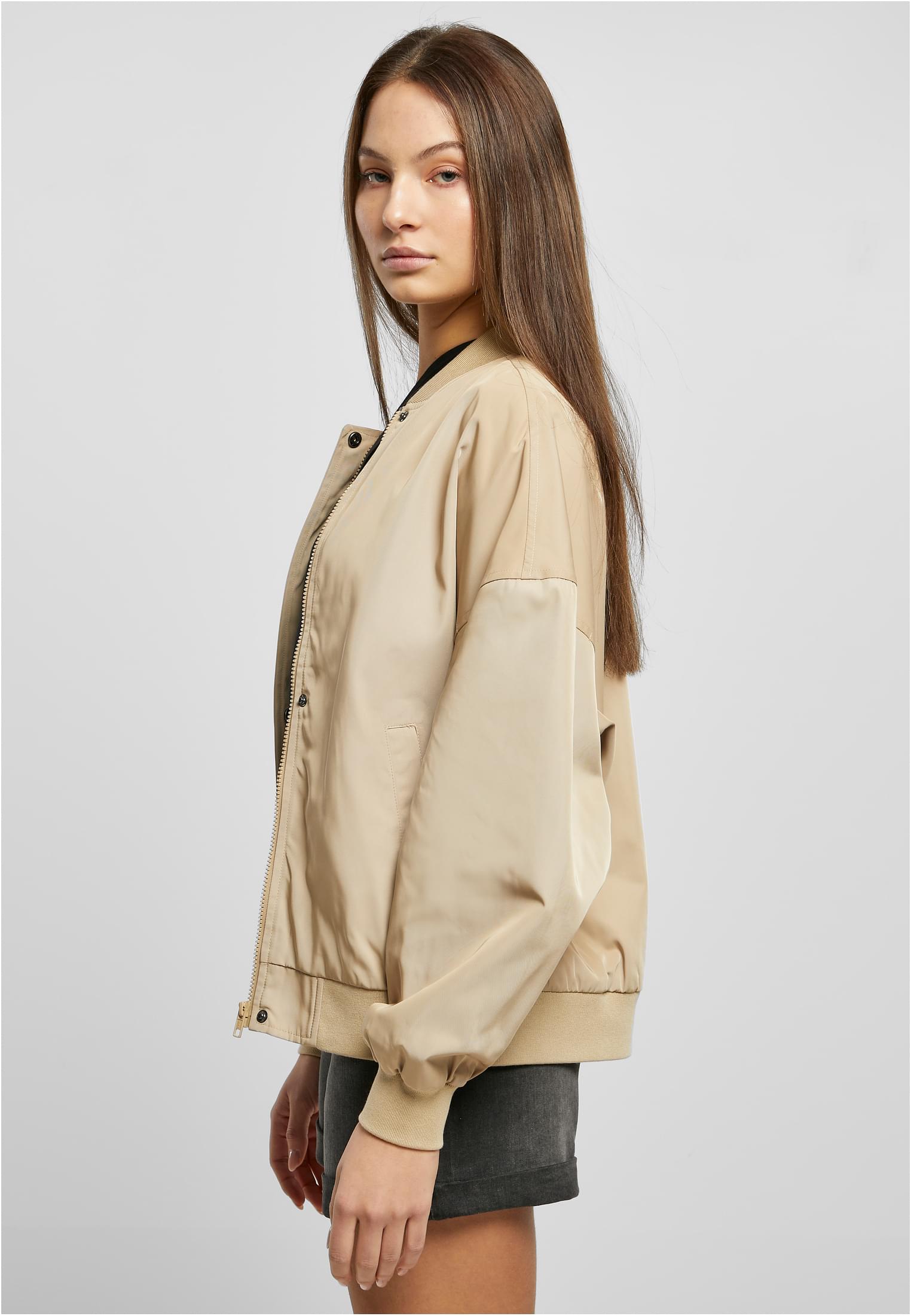 En kvinna sedd från sidan bär en beige UC Recycled Oversized Light Bomber Jacket.