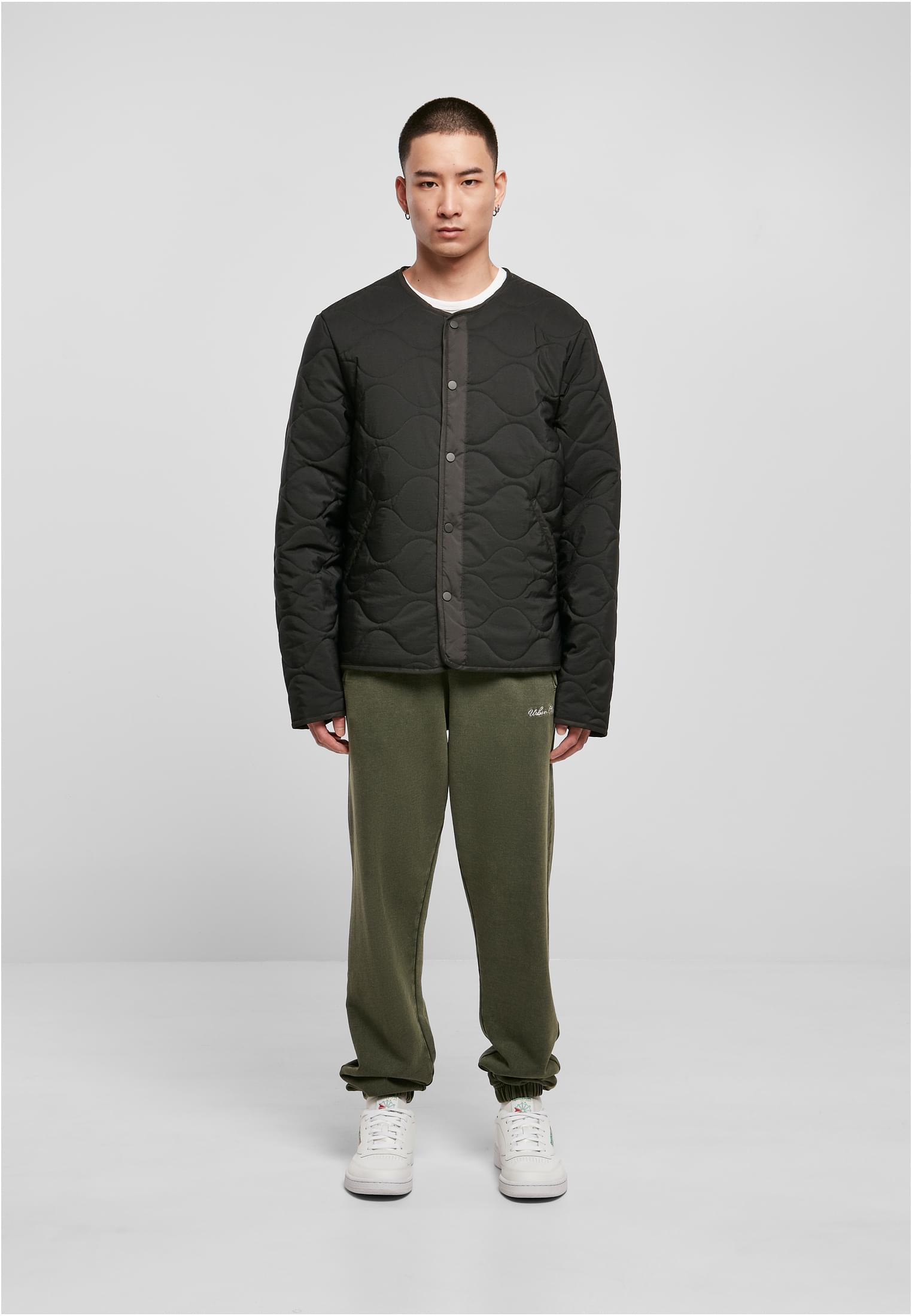 En man fotograferad framifrån, klädd i en svart quiltad UC Liner Jacket, gröna mjukisbyxor och vita sneakers.