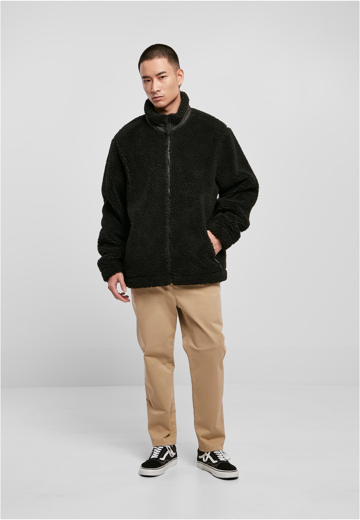 En manlig modell som bär en svart UC Basic Sherpa Jacket, stylad med beige byxor och svarta sneakers.