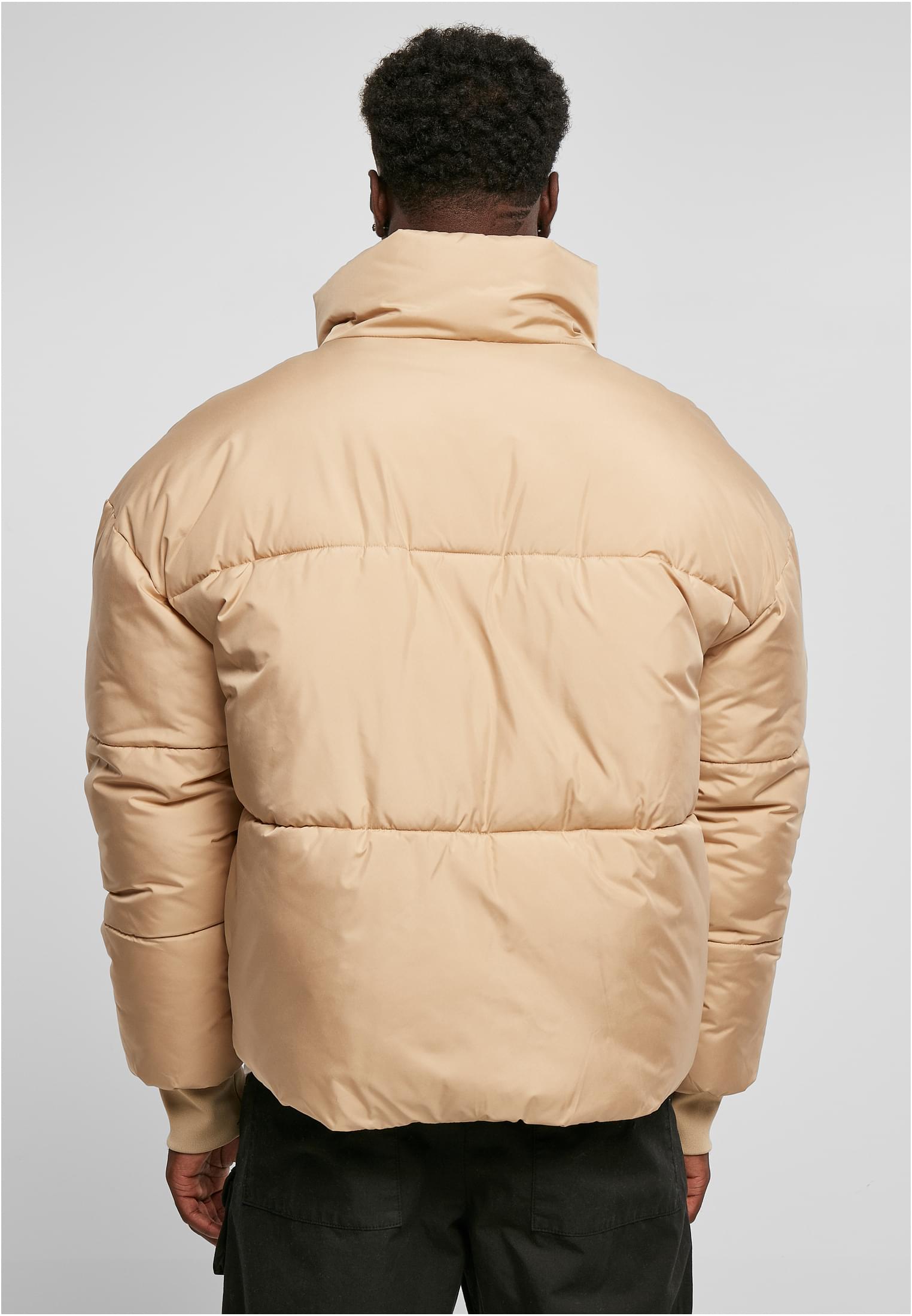 En man visar baksidan av en beige, oversized pufferjacka.