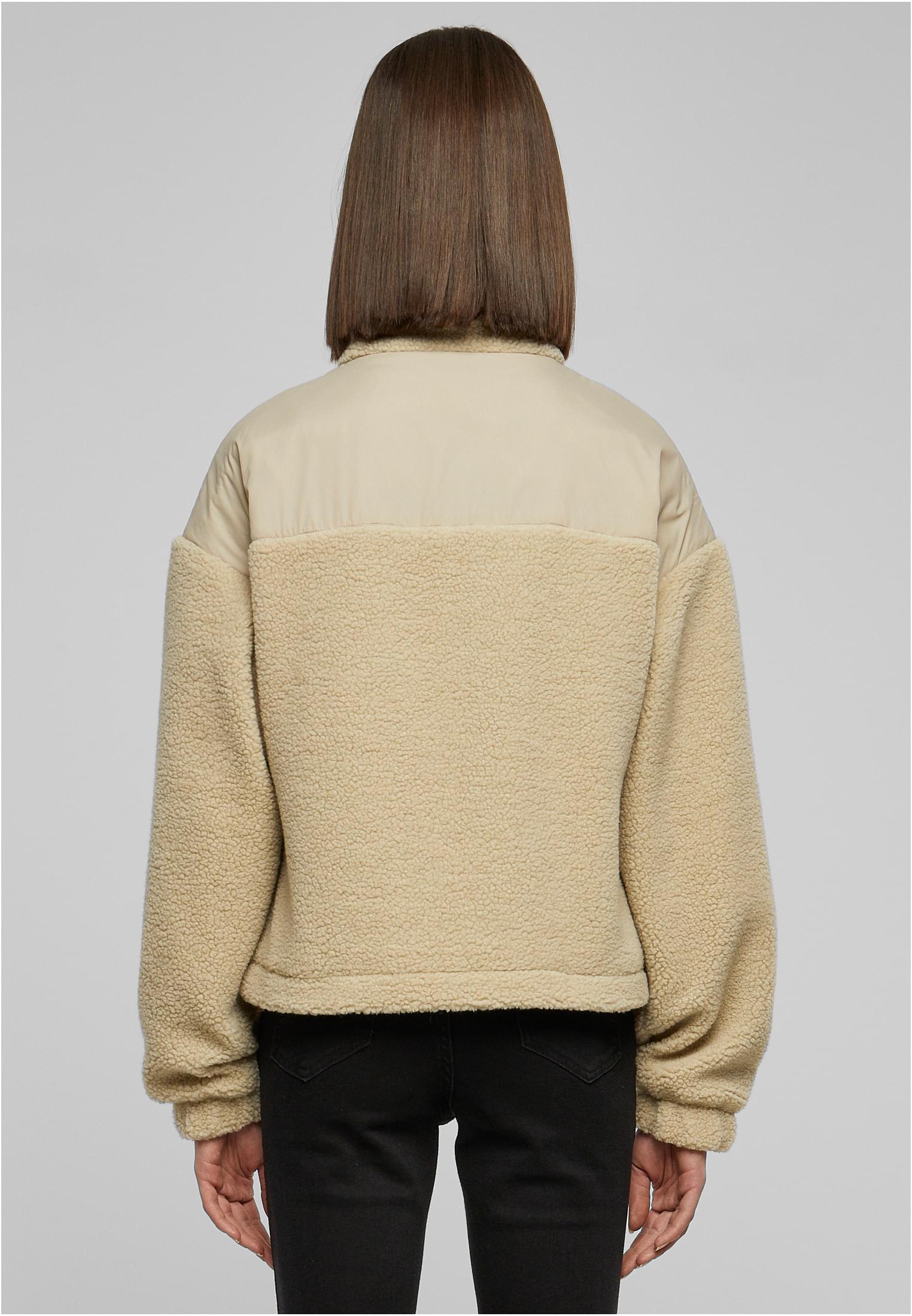 Baksidan av en kvinna som bär en beige sherpajacka med en nylonpanel över axlarna.