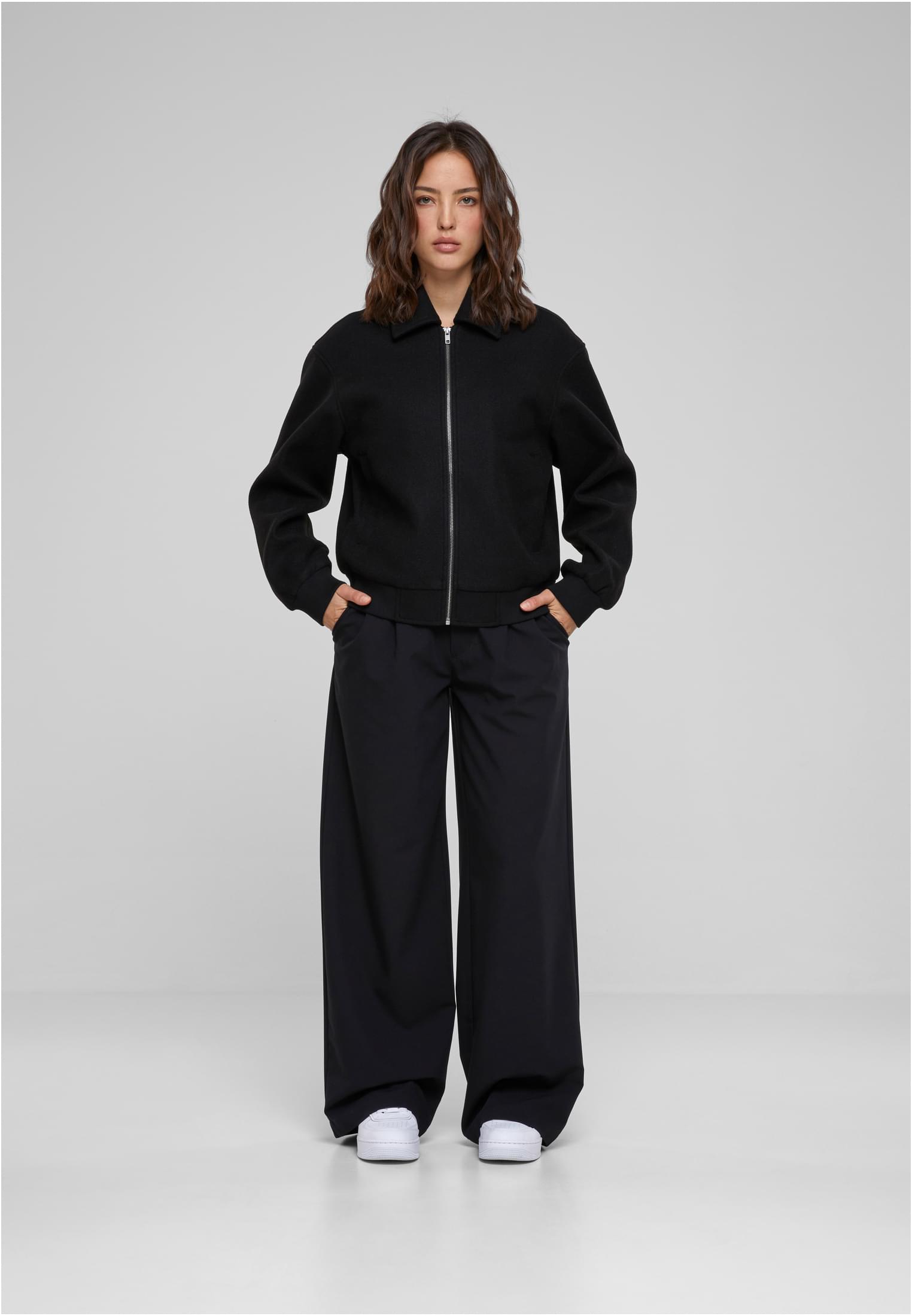 En kvinna visar framsidan av den svarta UC Boxy Jacket, stylad med vida svarta byxor och vita sneakers.