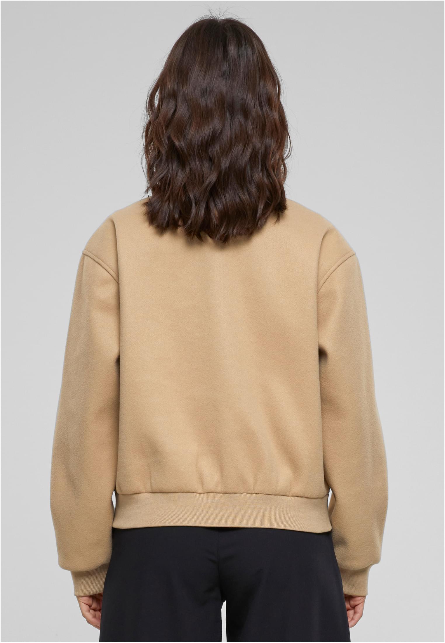 En kvinna visar baksidan av en beige, boxig bomberjacka.