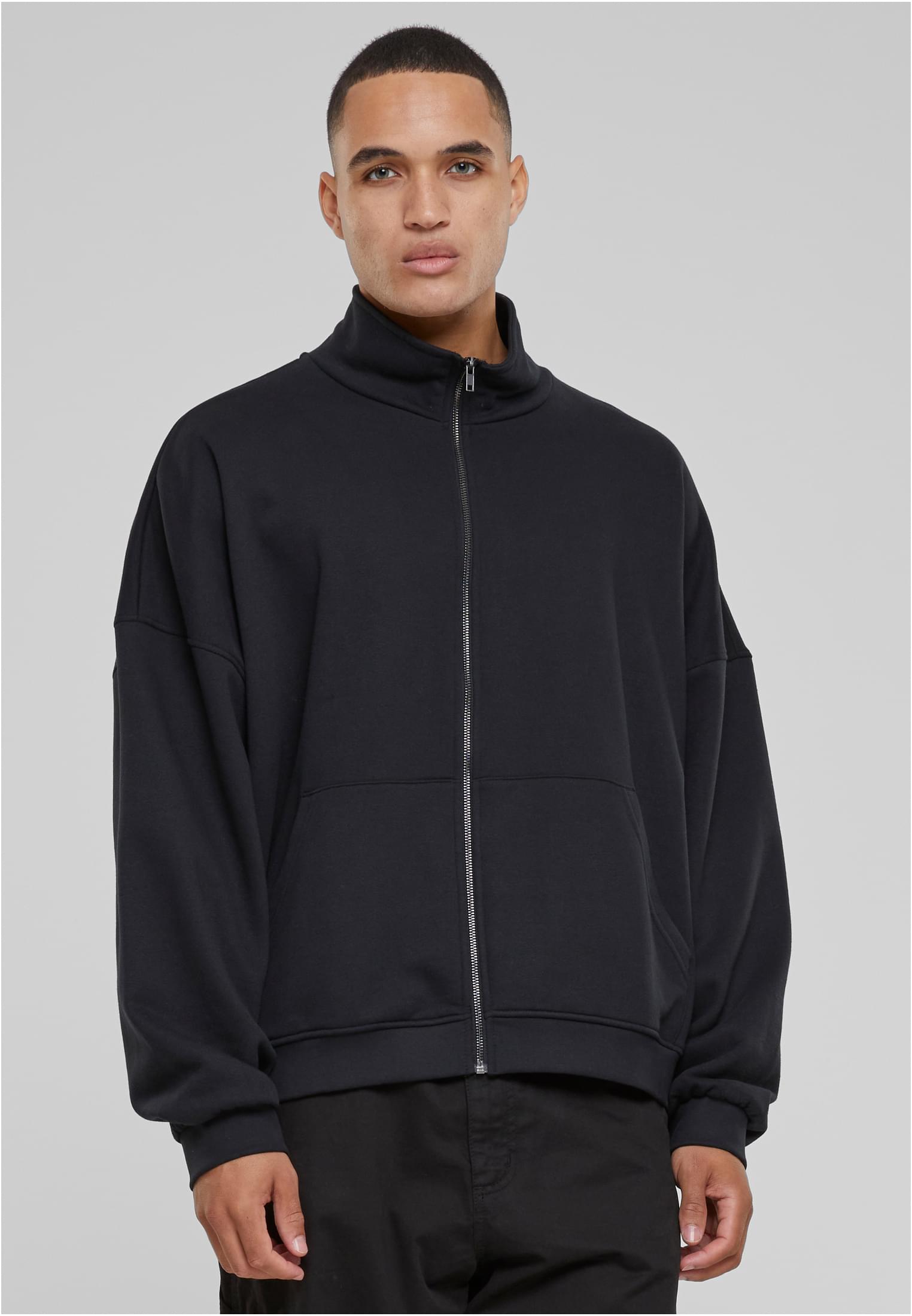 En man visar framsidan av en svart oversized 90-tals track jacket med hög krage.