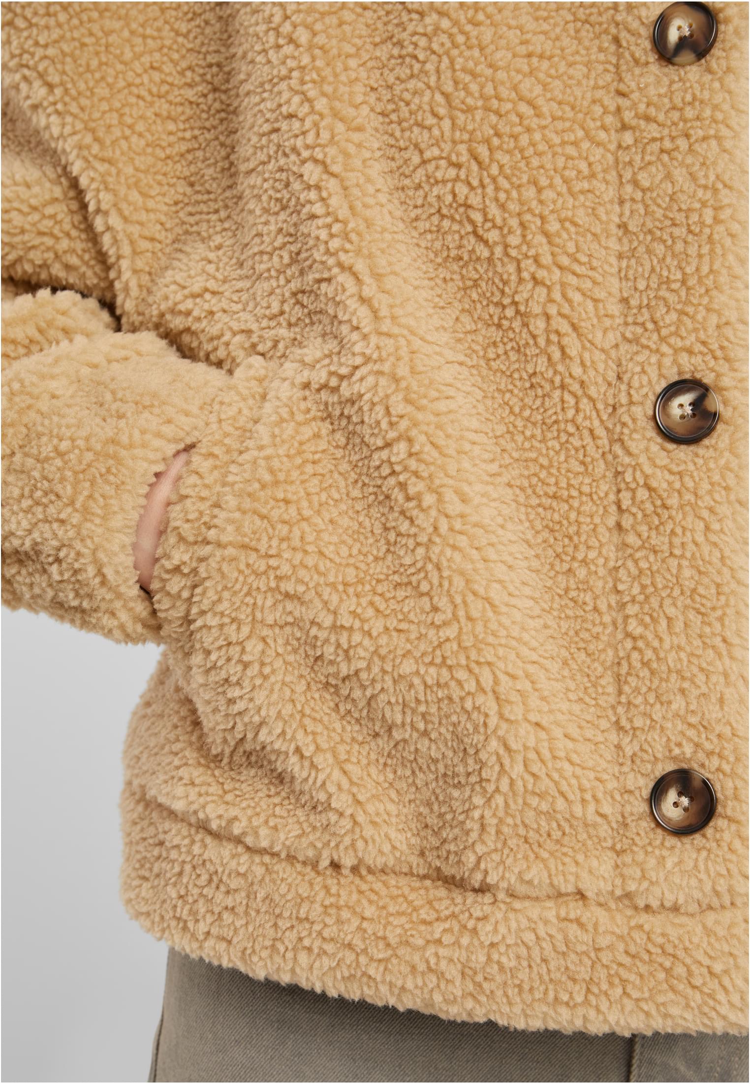 Närbild av en beige sherpajacka som visar den mjuka texturen, knapparna och en hand i sidofickan.