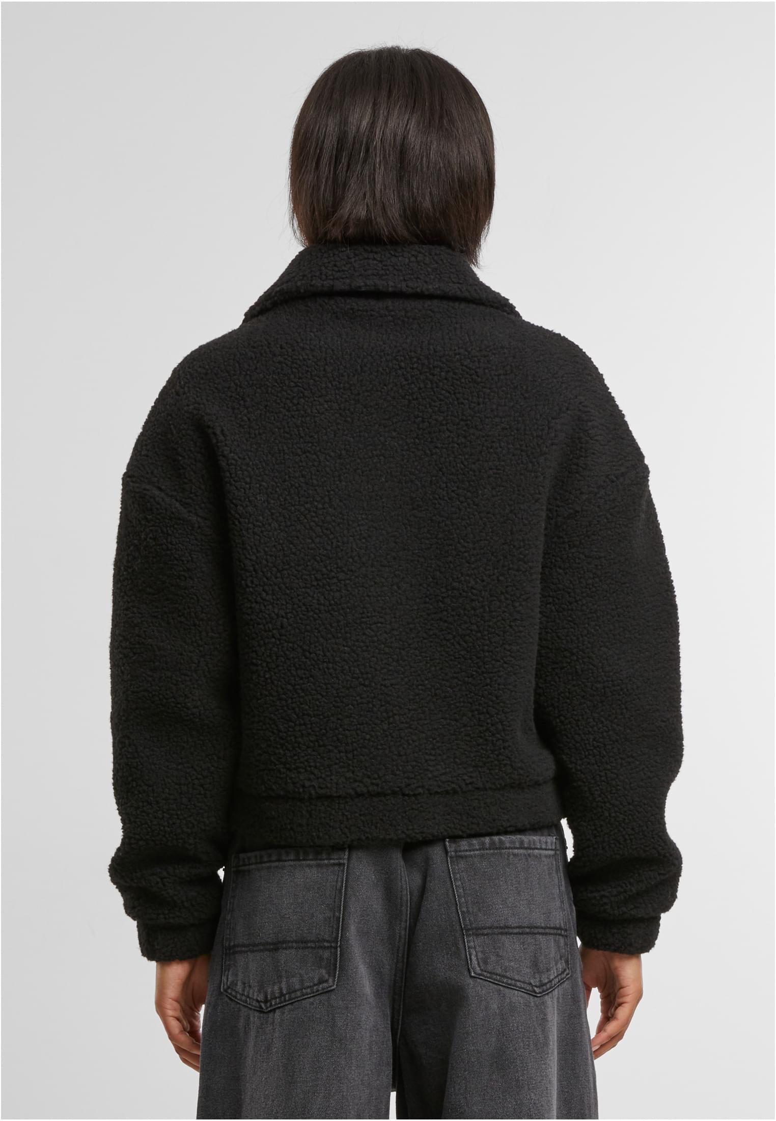 En kvinna visar baksidan av en kort, svart sherpajacka.