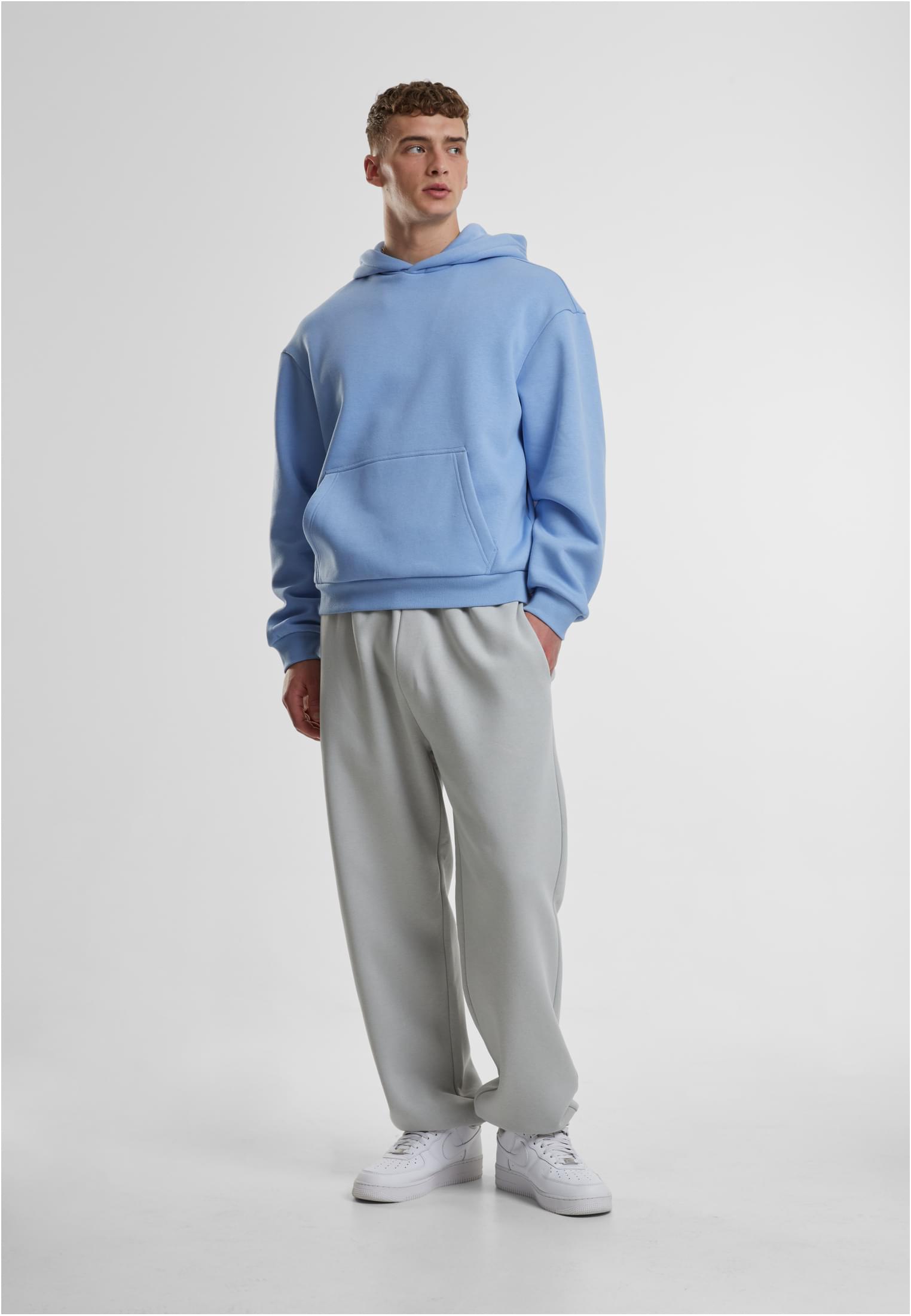 Manlig modell som bär ljusgrå Fluffy Sweatpants, stylade med en ljusblå hoodie och vita sneakers mot en vit bakgrund.