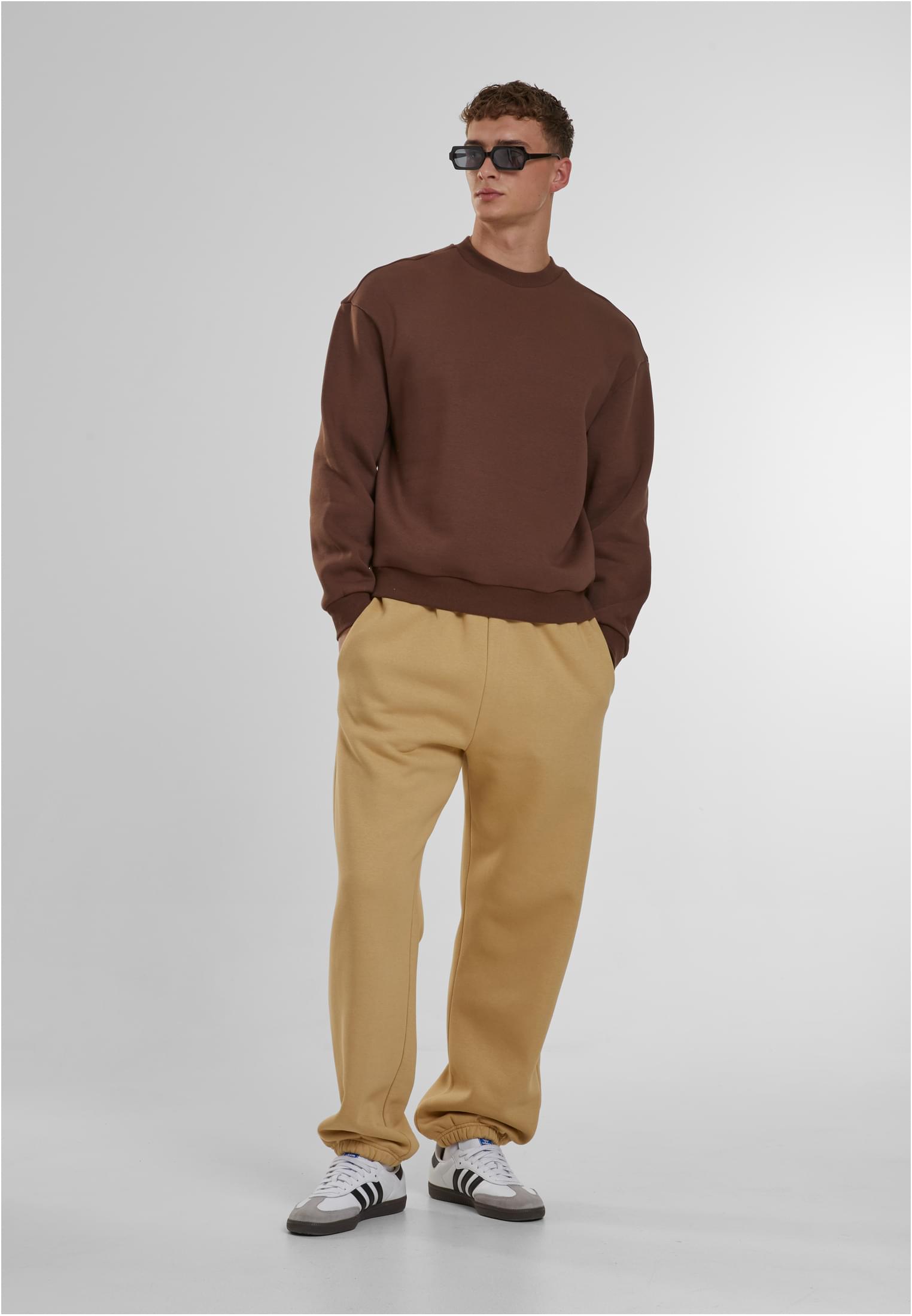 Manlig modell som bär beiga Fluffy Sweatpants, en brun sweatshirt och solglasögon.