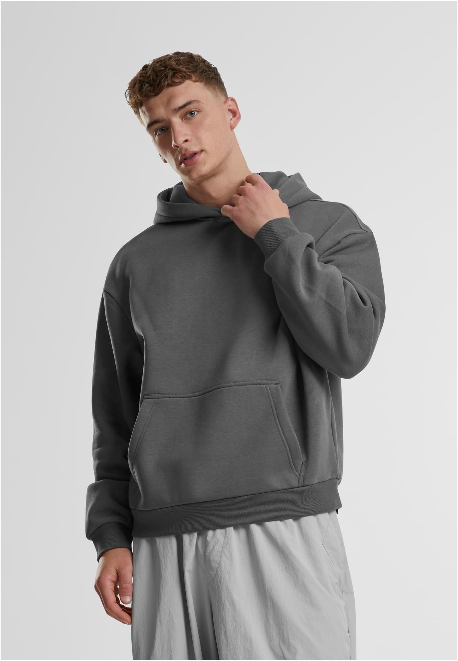 En manlig modell poserar i en mörkgrå Fluffy Hoody mot en vit bakgrund.