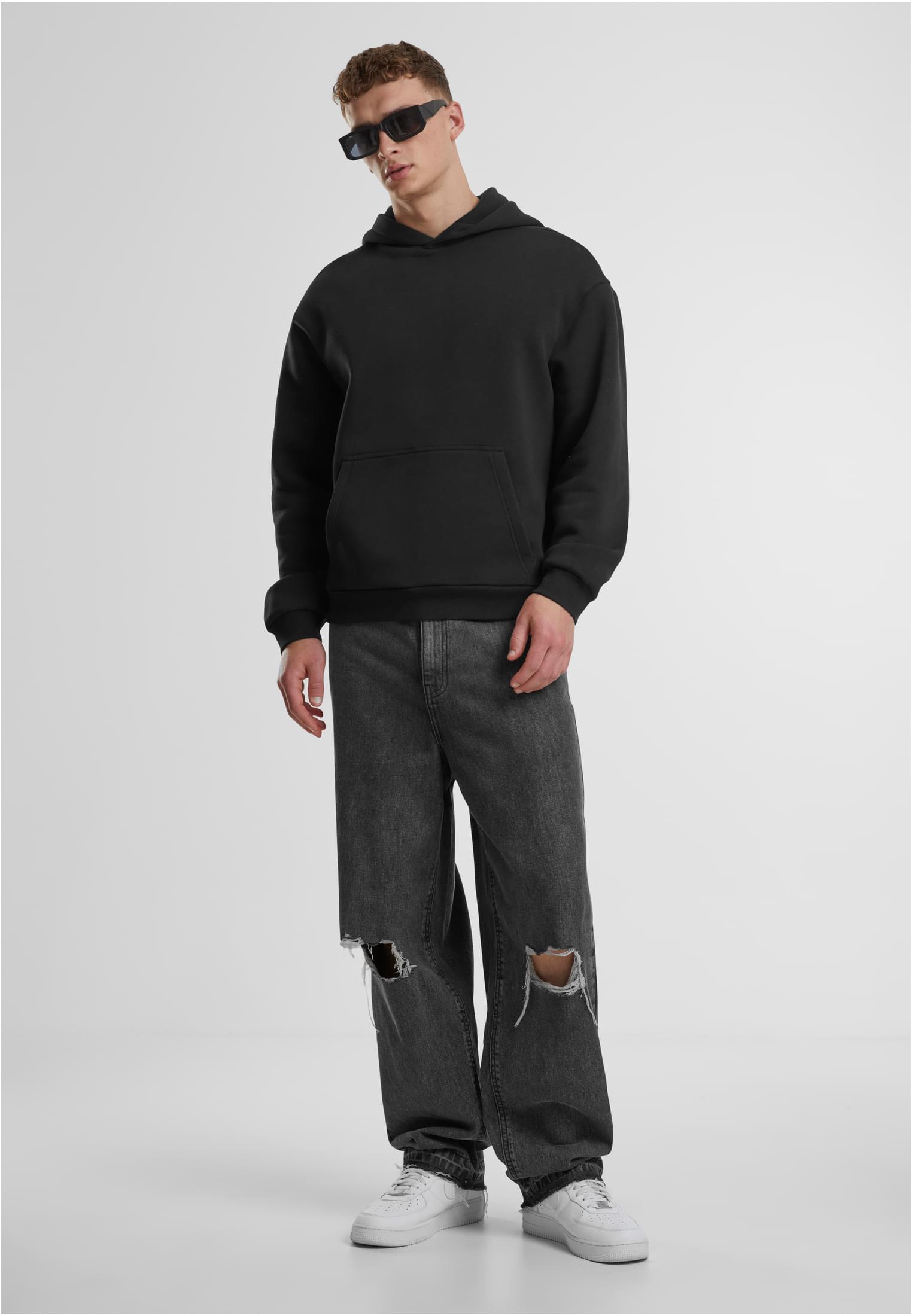 En manlig modell klädd i en svart luvtröja, mörkgrå slitna jeans och solglasögon.