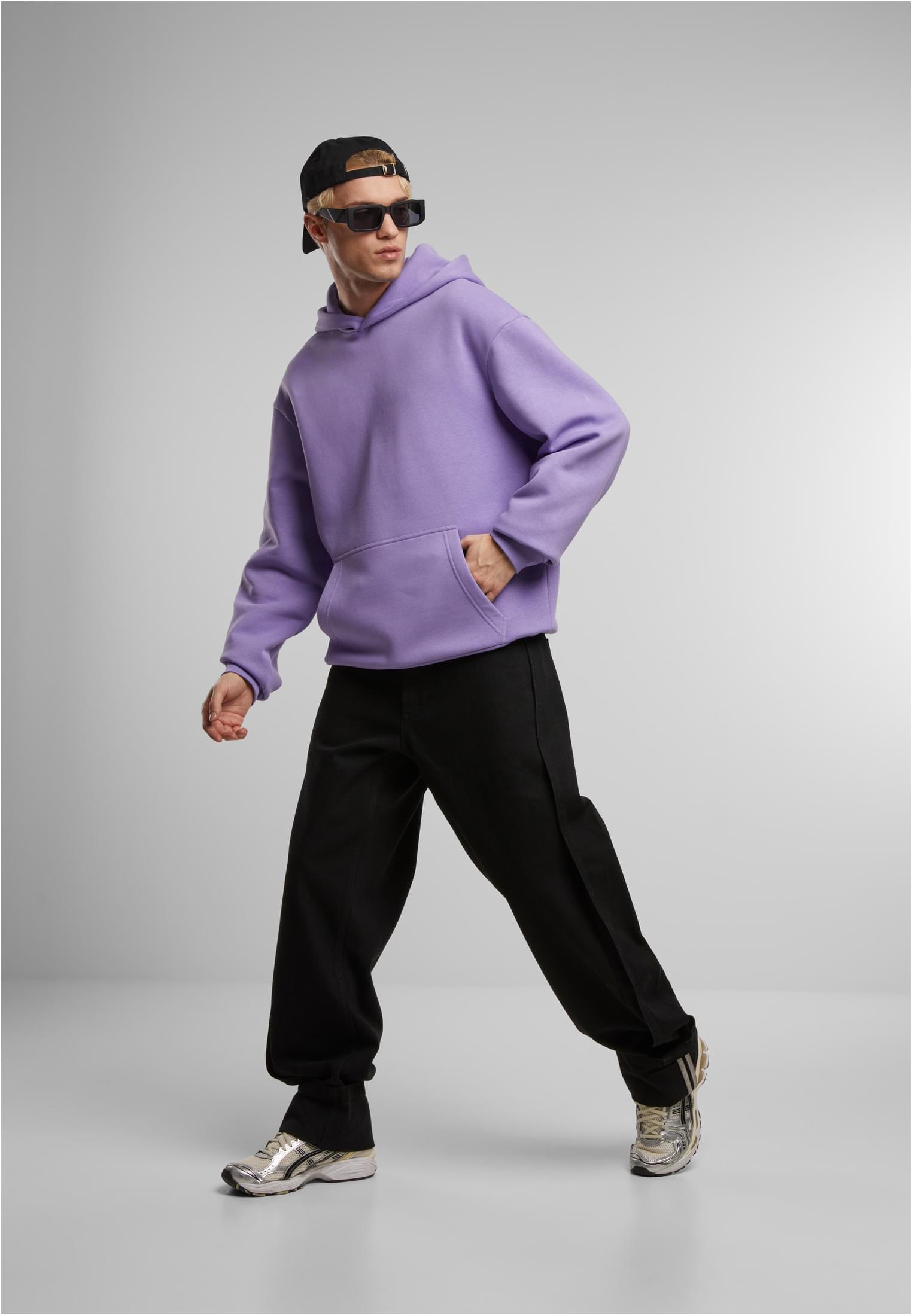 Manlig modell i lila Fluffy Hoody, svarta byxor, svart keps och solglasögon.