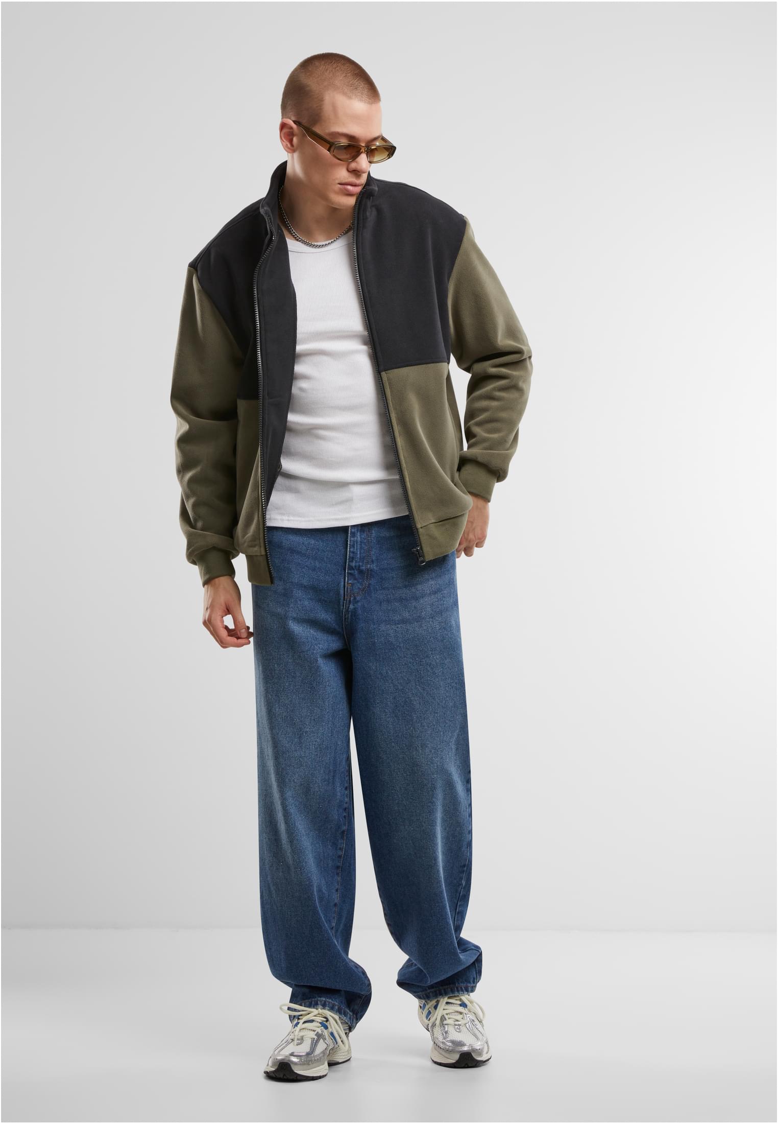 En manlig modell poserar i en färgblockerad polarfleecejacka i olivgrönt och svart, tillsammans med en vit t-shirt och vida blåjeans.