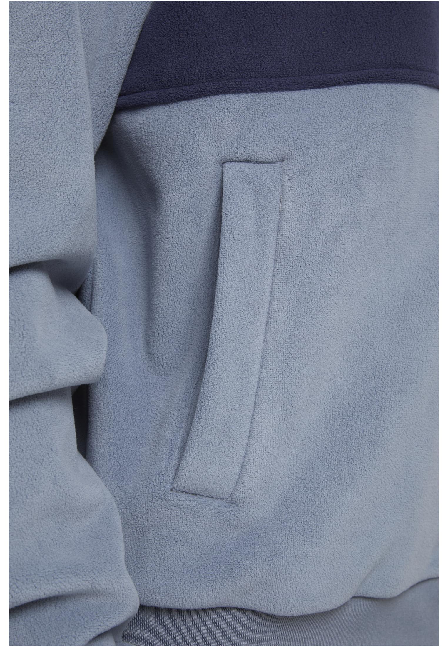 Detaljbild på en ljusblå och mörkblå fleecejacka som visar sidofickan och tygets struktur.