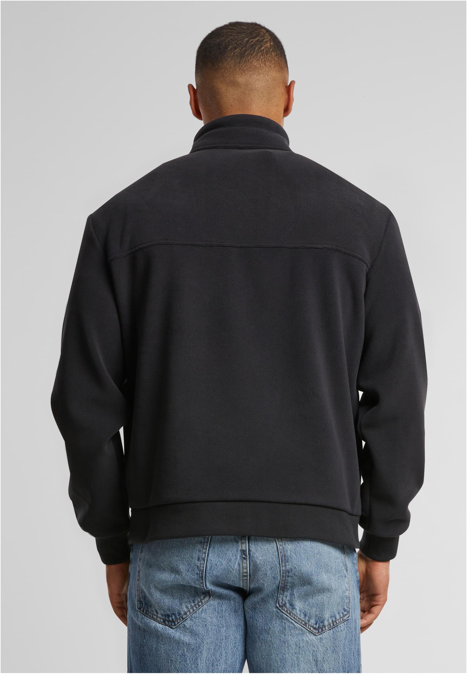 En man visar baksidan av en svart UC Colour Block Polar Fleece-jacka.
