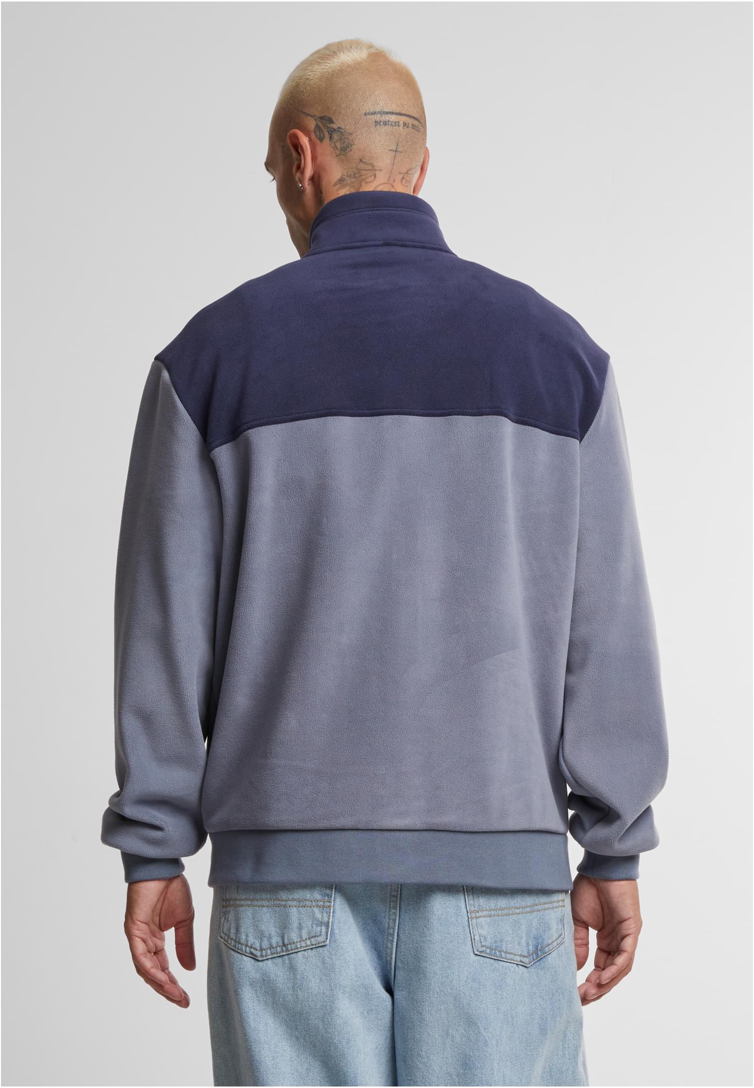 En man visar baksidan av en färgblockerad polarfleecejacka i blå nyanser.