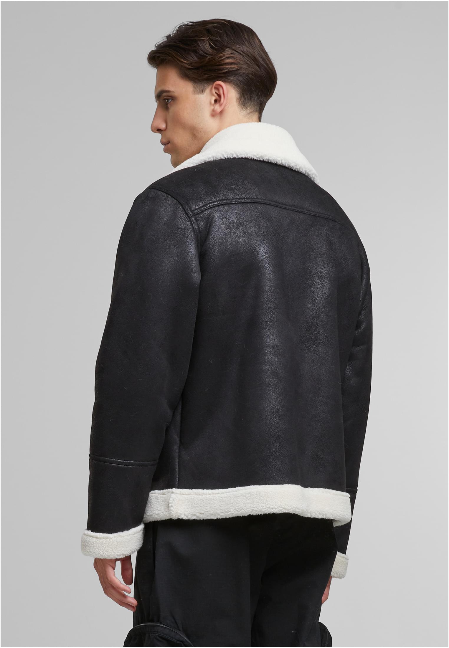 En man, sedd snett bakifrån, bär en svart UC Shearling Biker Jacket med vit krage och foder.