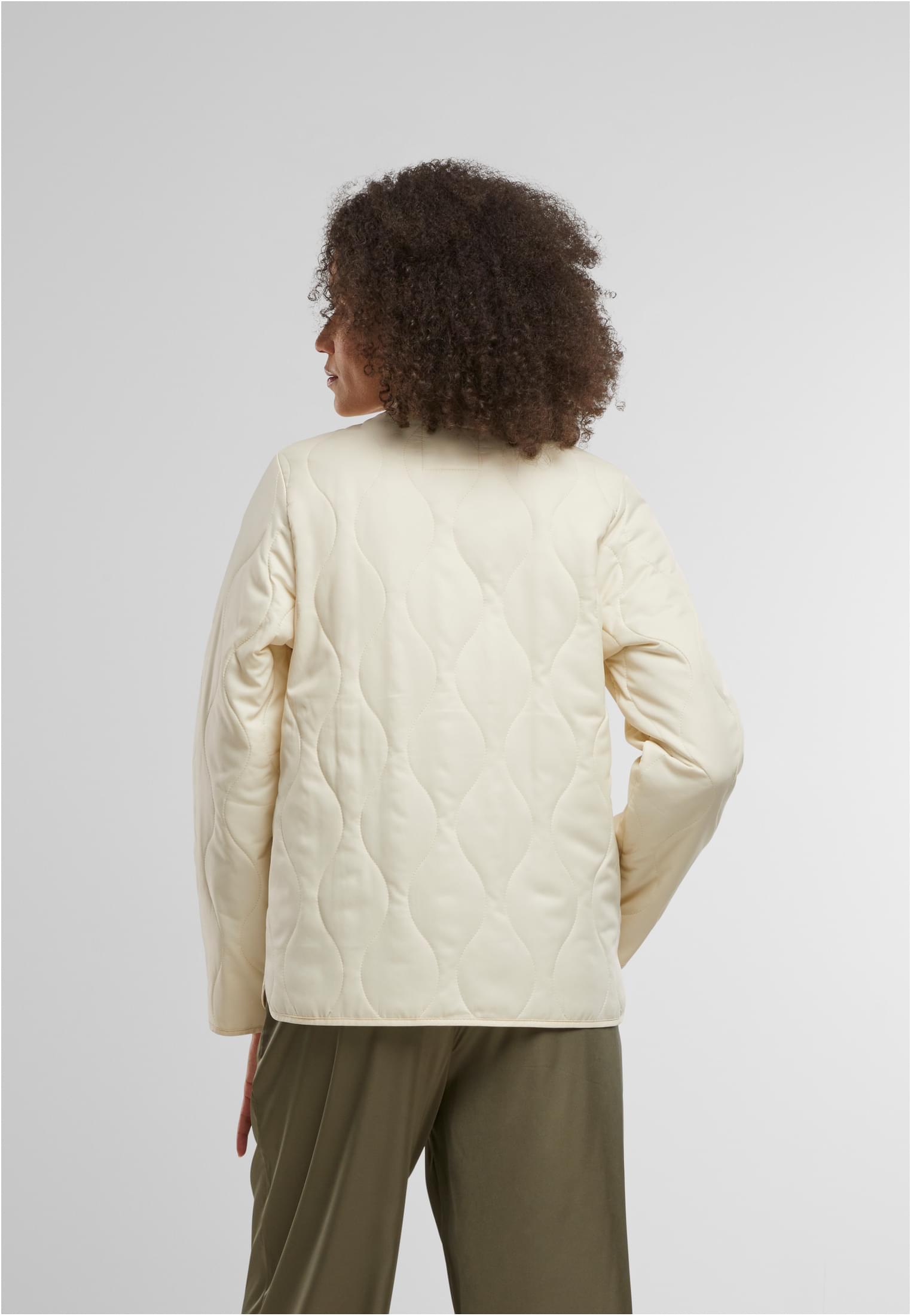 En kvinna visar baksidan av en beige, quiltad jacka.