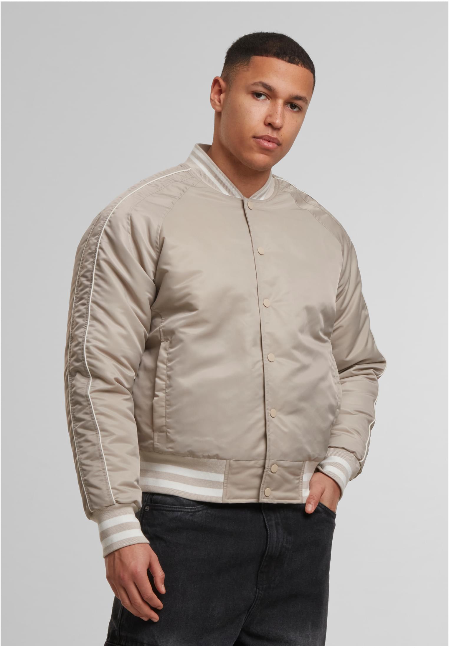 En manlig modell visar framsidan av en beige UC Racer Bomber Jacka med vita ränder på muddar och krage.