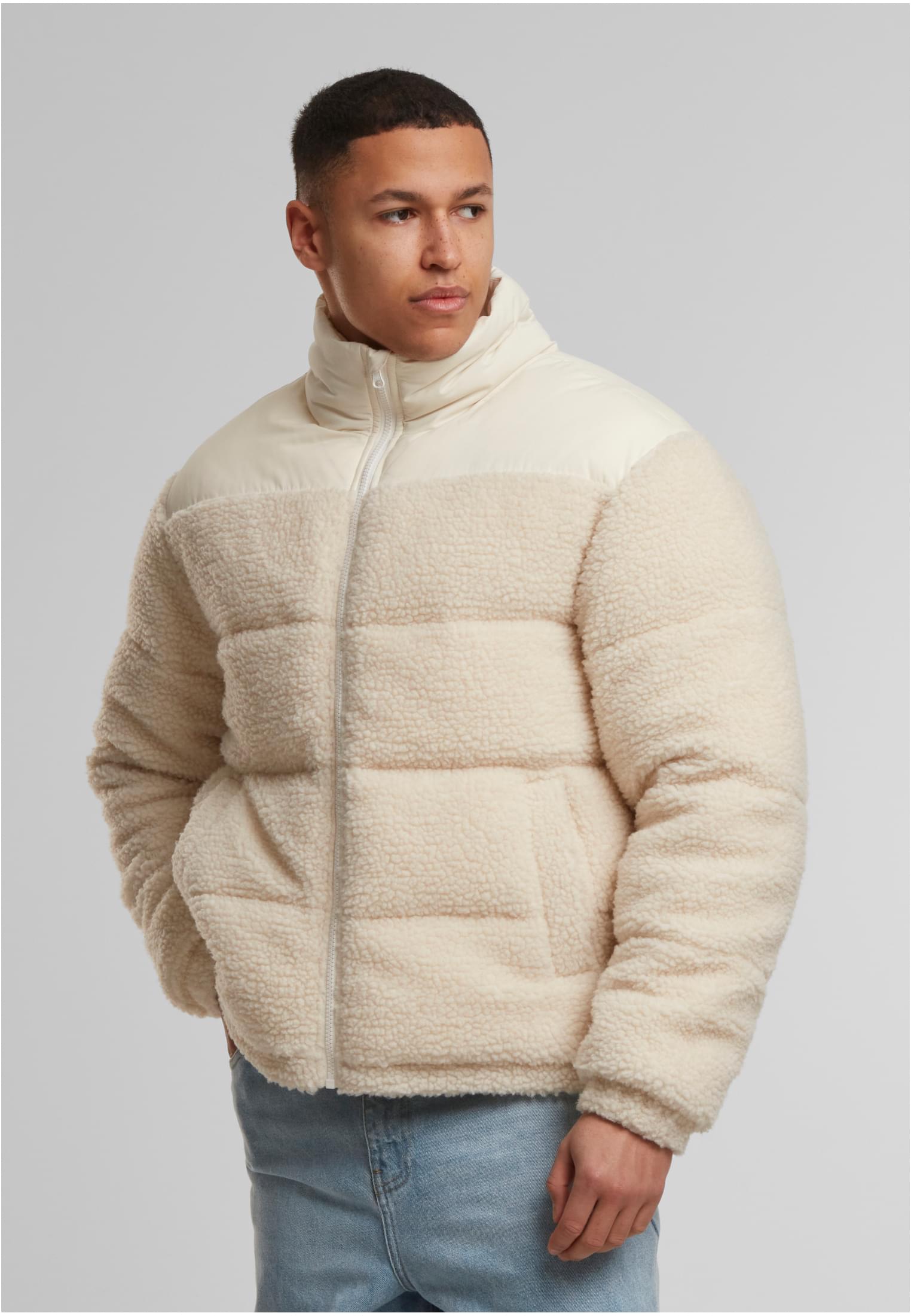 En man visar framsidan av en beige puffjacka med teddyfleece.