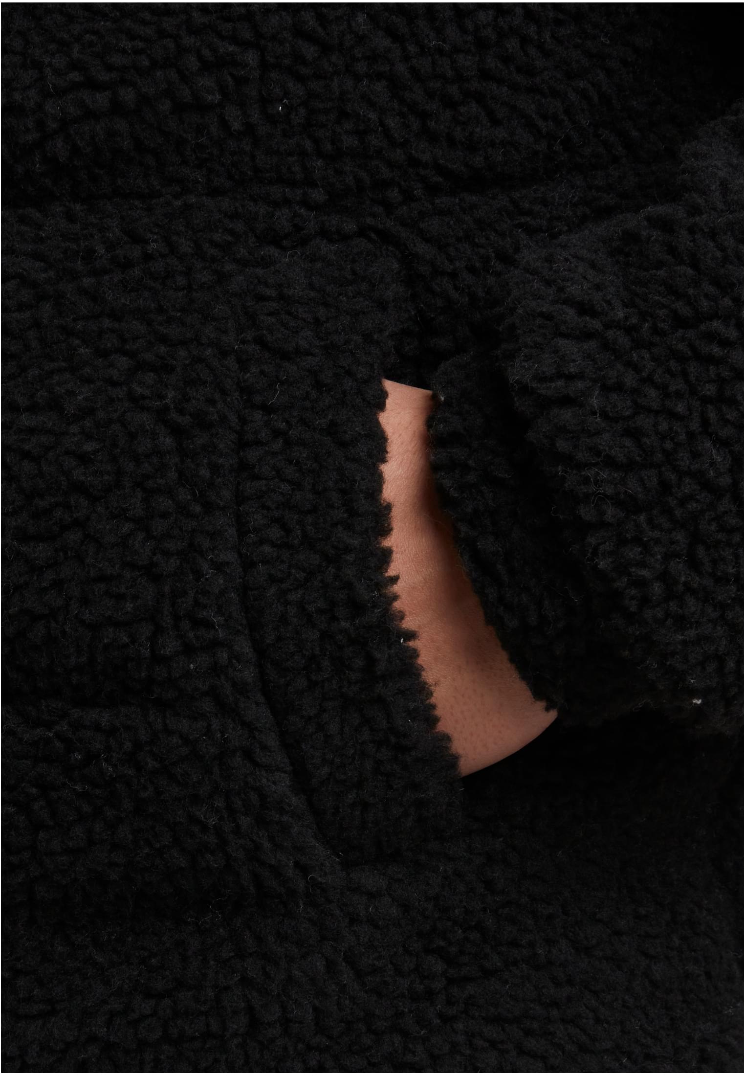 Närbild på fickan och materialet på en svart teddyfleecejacka.