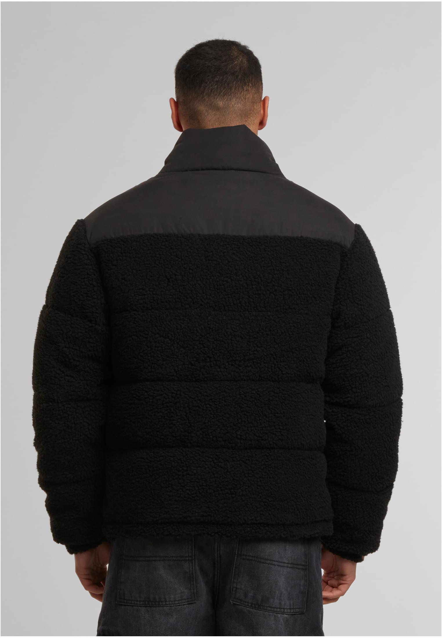 En man, sedd bakifrån, bär en svart pufferjacka med teddyfleece.