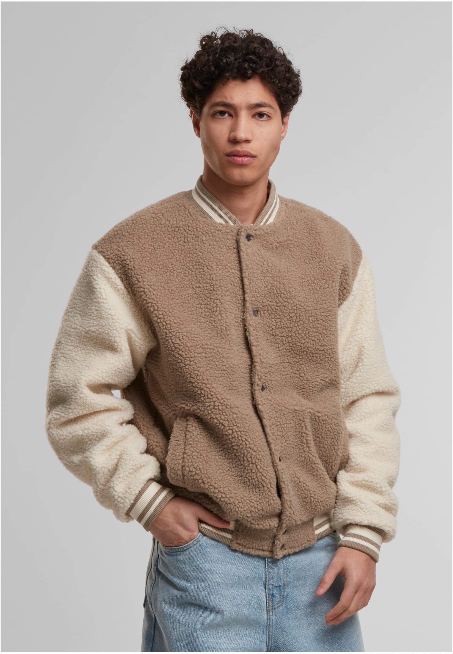 En man som bär en Teddy College Jacket i mörk taupe med benvita ärmar.