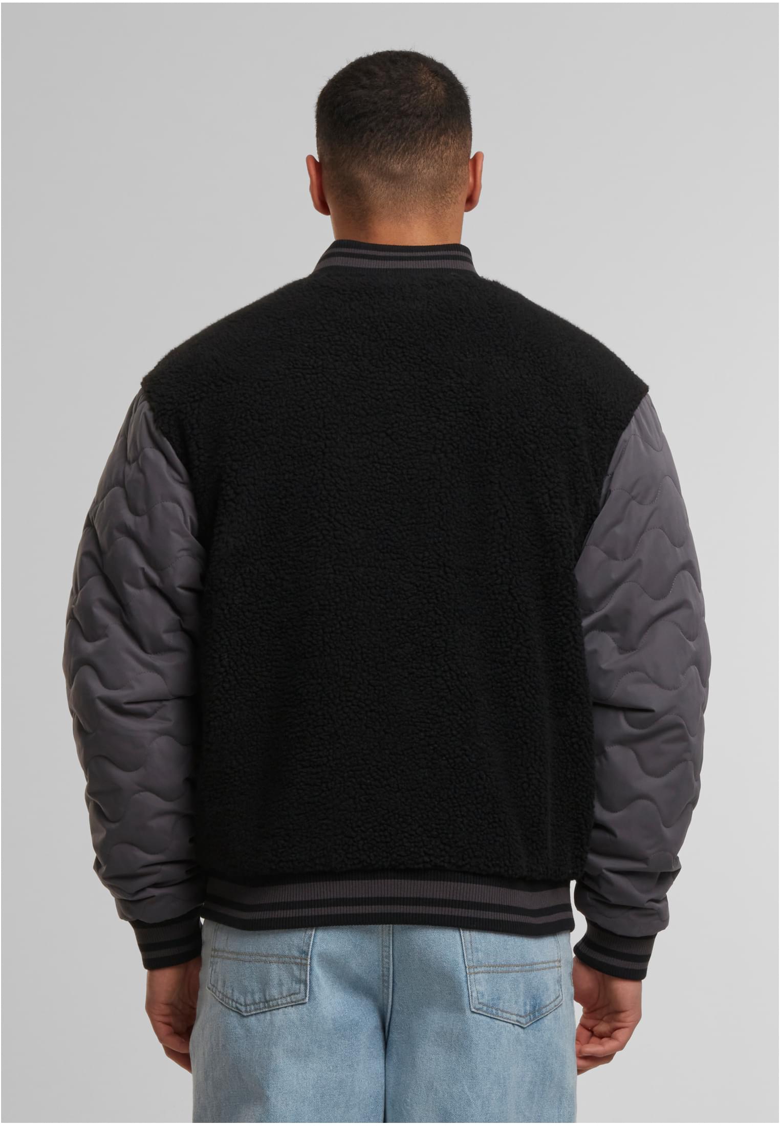 Baksidan av en man som bär en collegejacka med svart teddyfleece på kroppen och mörkgrå quiltade ärmar.