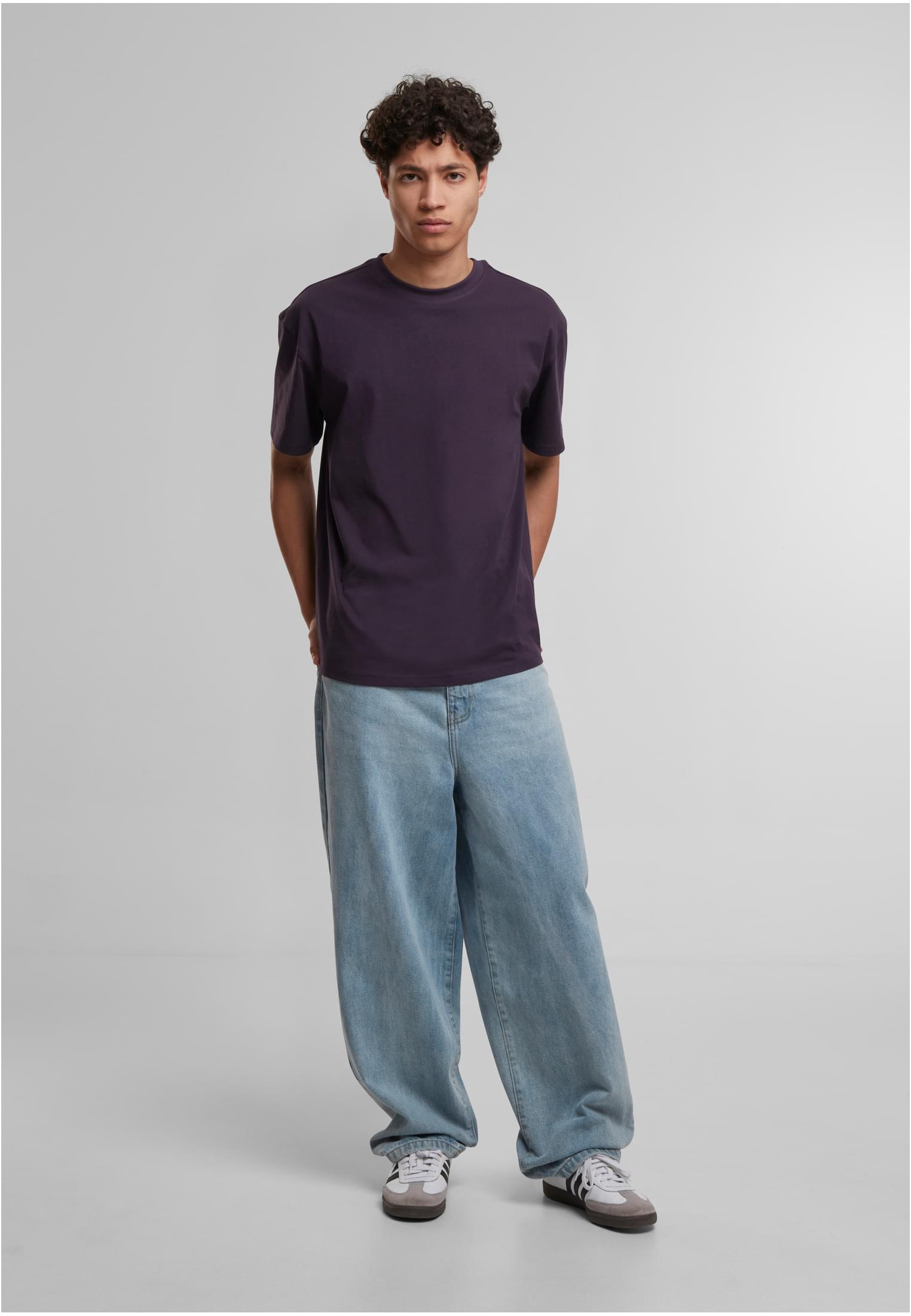 En man bär en mörklila t-shirt med lös passform och vida ljusblåa jeans.