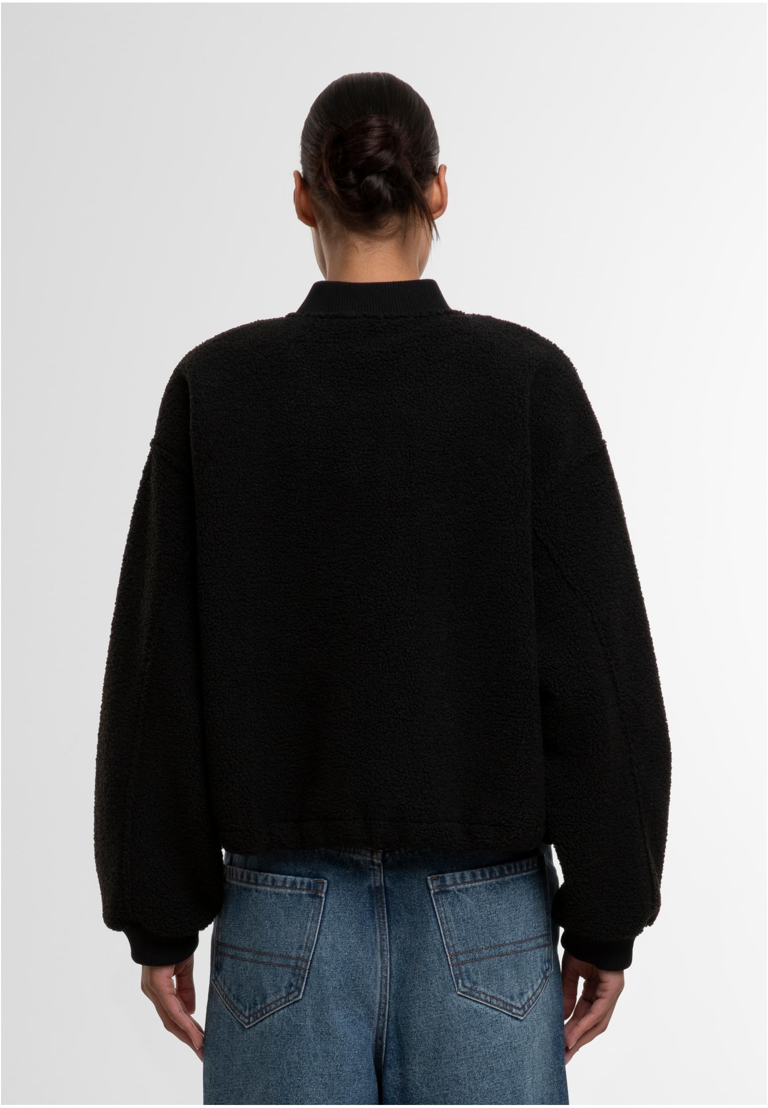 En kvinna visar baksidan av en svart, strukturerad bomberjacka.