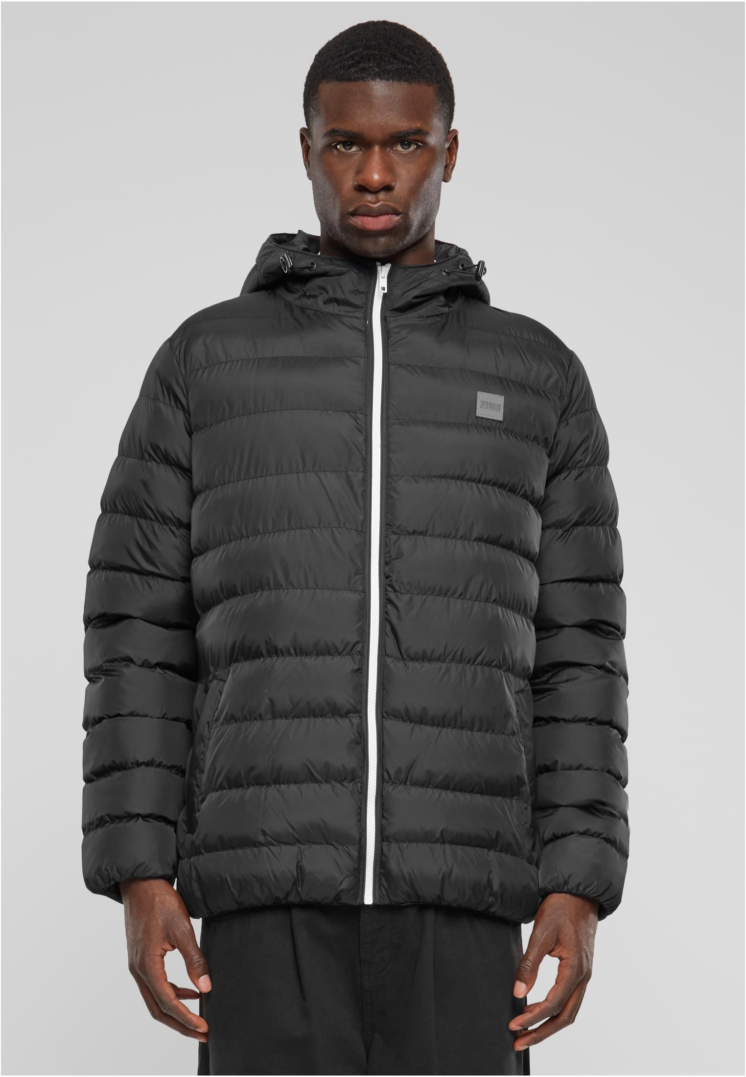 En man visar framsidan av en svart, vadderad jacka med huva och en vit dragkedja.