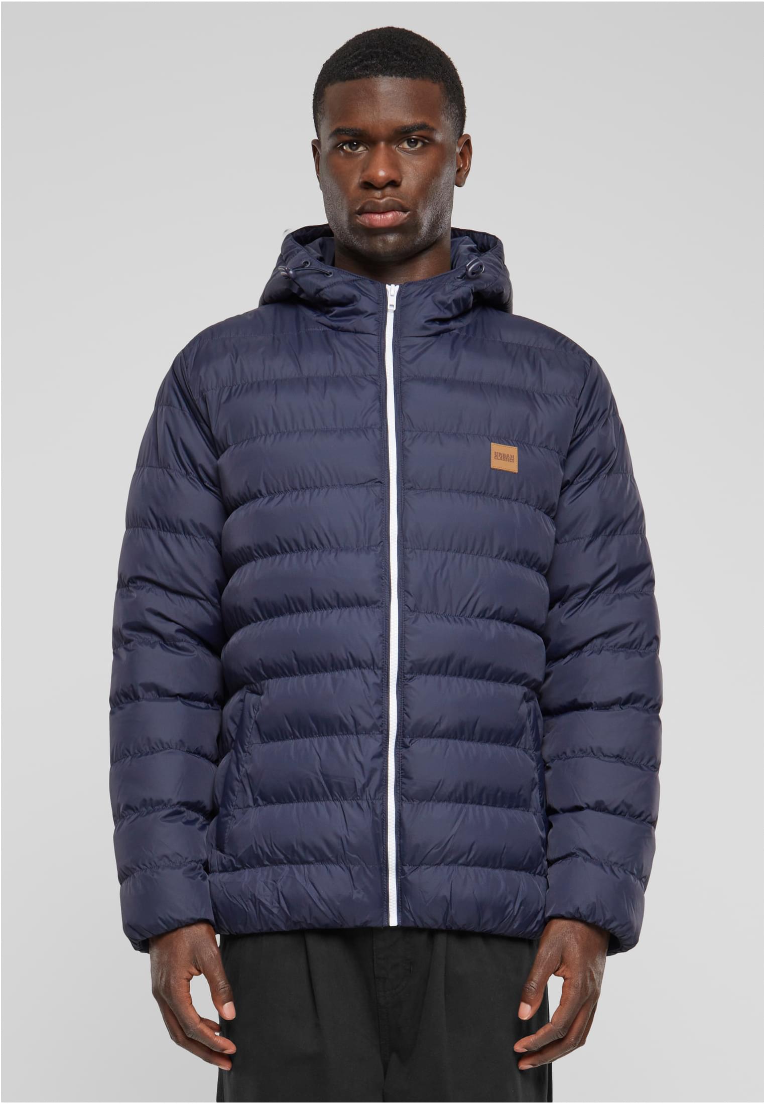 En man visar framsidan av en mörkblå, quiltad bubbeljacka med huva och vit dragkedja.