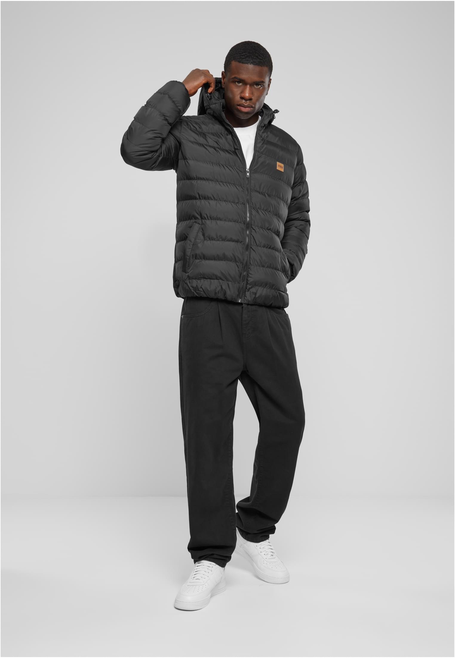 En man som bär den svarta UC Basic Bubble Jacket, svarta byxor och vita sneakers, stående framifrån medan han justerar huvan.