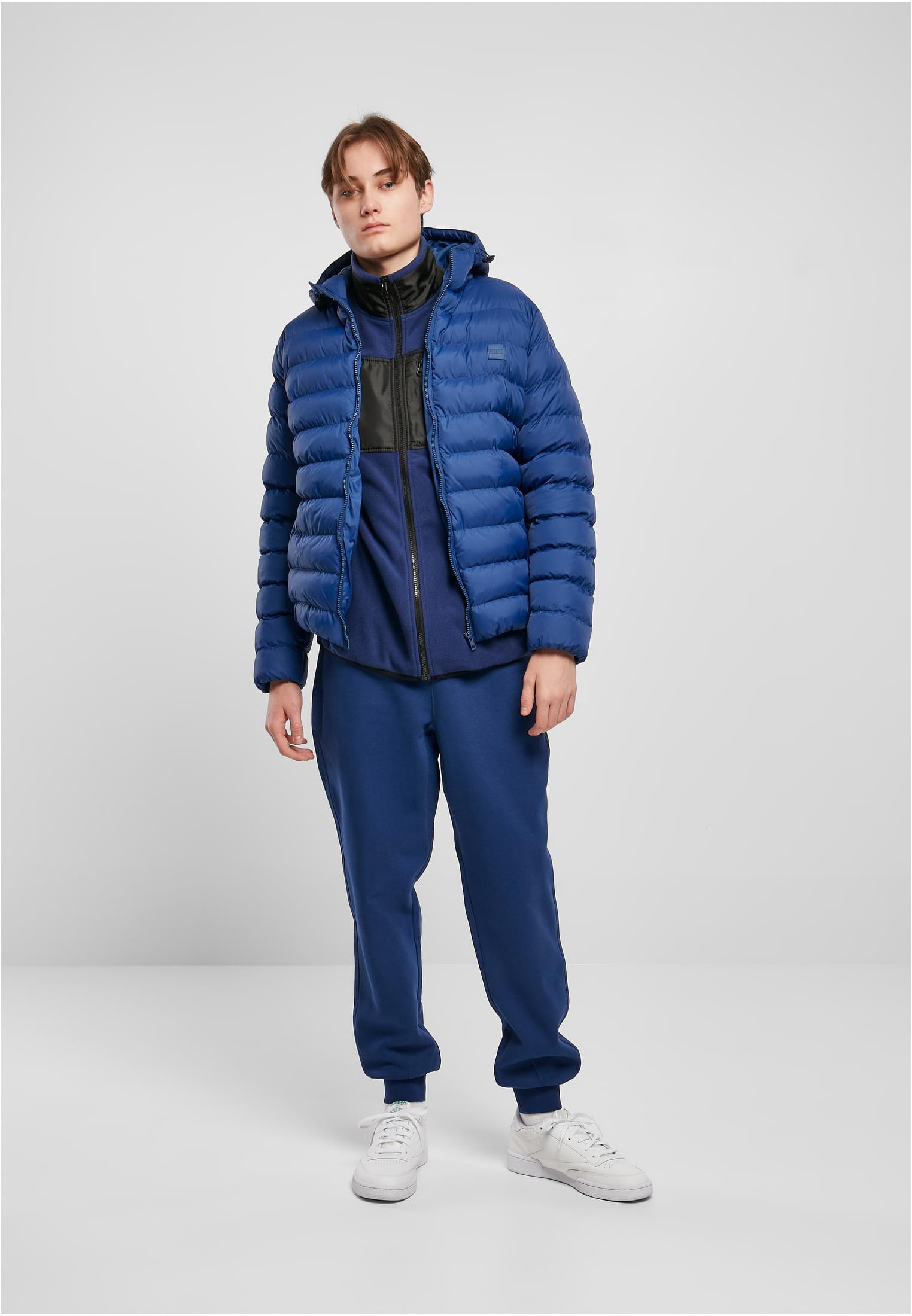 Manlig modell som visar framsidan av den blå UC Basic Bubble Jacket, stylad med en mörkblå fleecetröja och joggingbyxor.