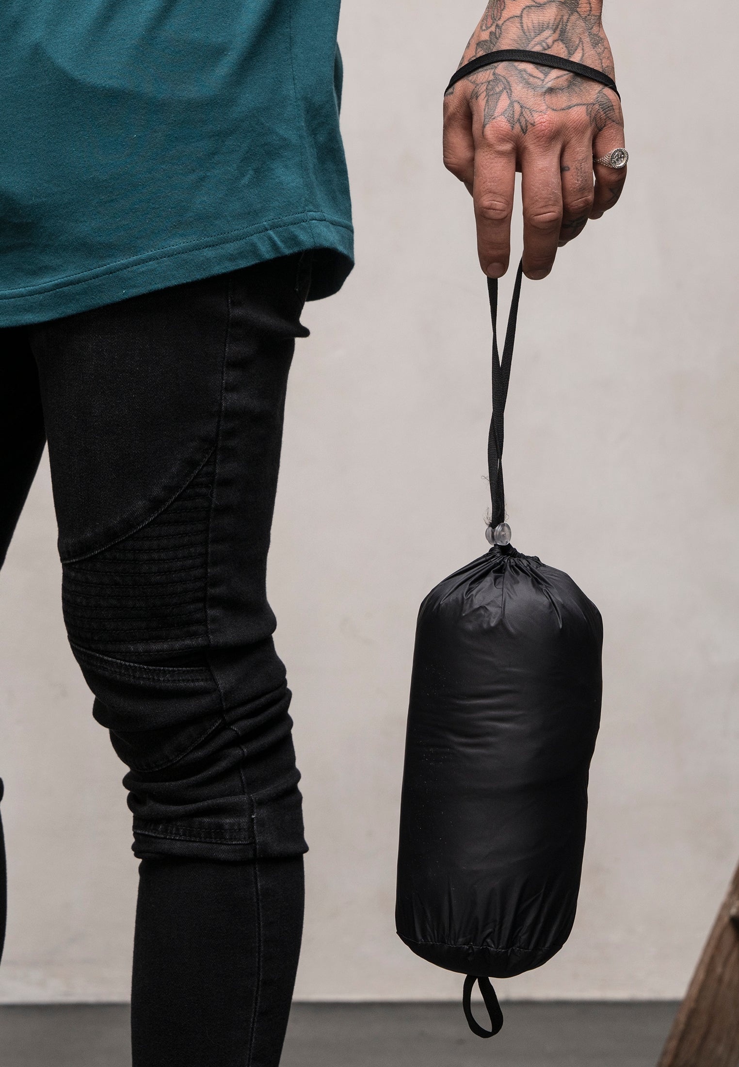 Detaljbild på en man som håller i den svarta förvaringspåsen till dunjackan UC Basic Hooded Down Jacket.