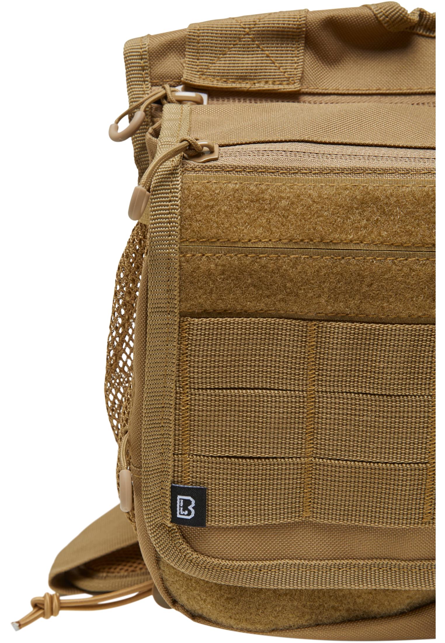 Närbild på en kamelfärgad B Travel Side Bag som visar materialets textur, fästpunkter, en kardborrepanel och märkets logotyp.