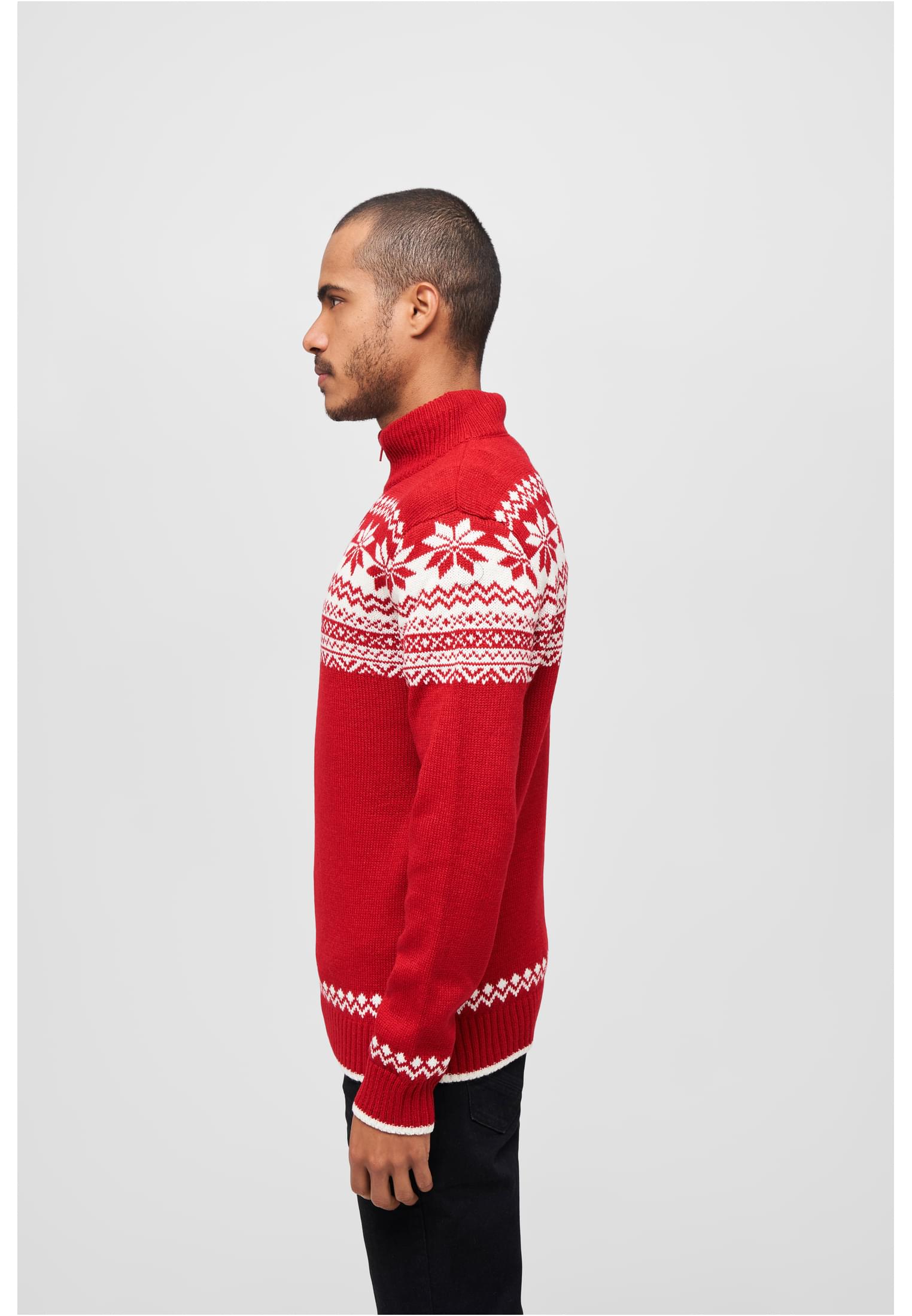 En man i sidoprofil som bär en röd stickad tröja med vitt norskt mönster.