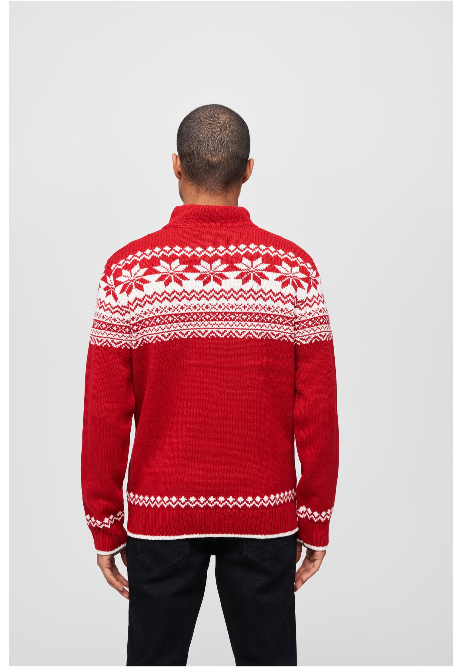 En man visar baksidan av en röd stickad tröja med vitt norskt mönster.