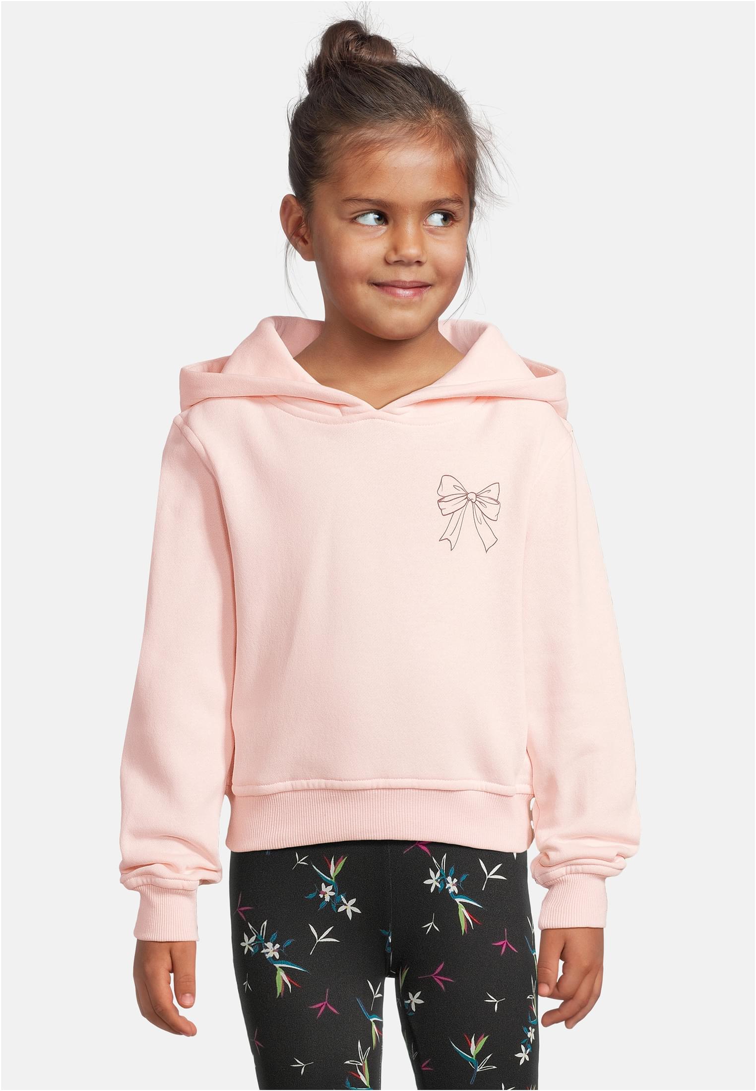 En ung flicka bär en rosa luvtröja med ett tryck av en rosett på bröstet.