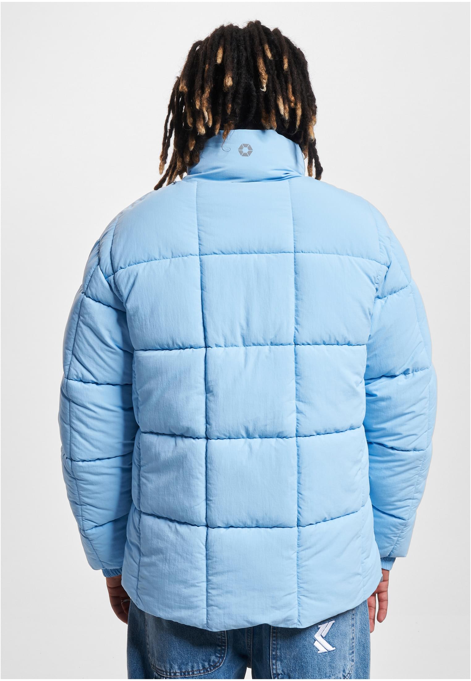 En man visar baksidan av en ljusblå, quiltad pufferjacka.