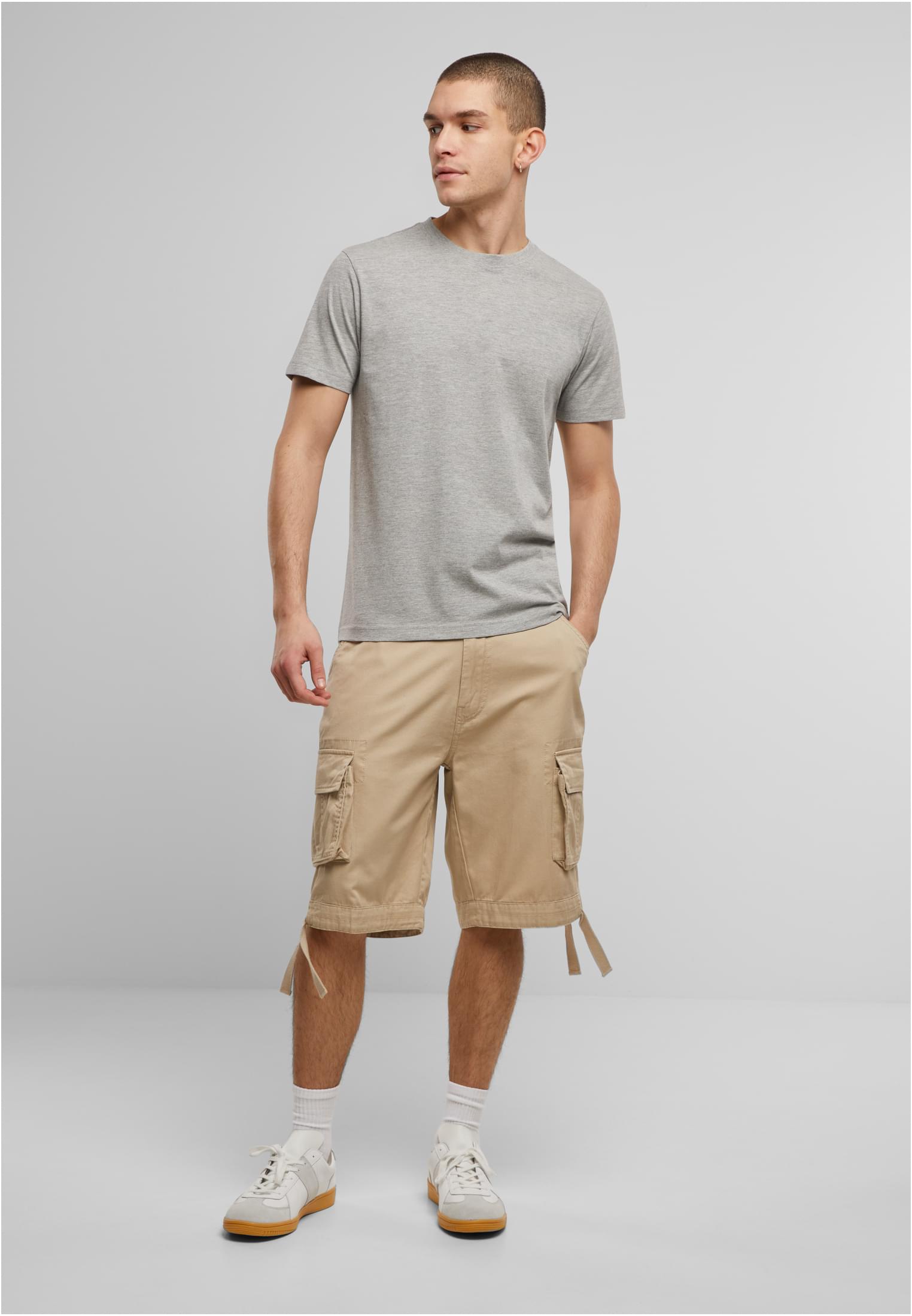 En manlig modell i en grå t-shirt, beiga cargoshorts och vita sneakers.