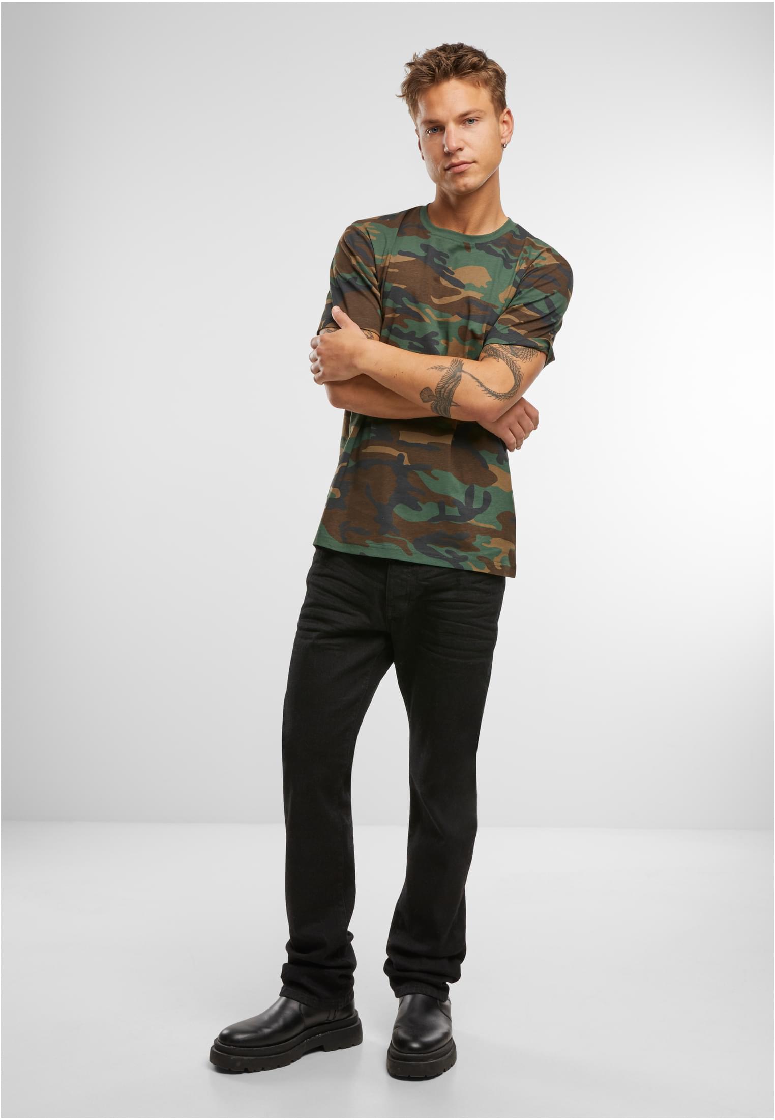 En manlig modell poserar i en kamouflagemönstrad Brandit Premium Shirt, svarta jeans och svarta skor.