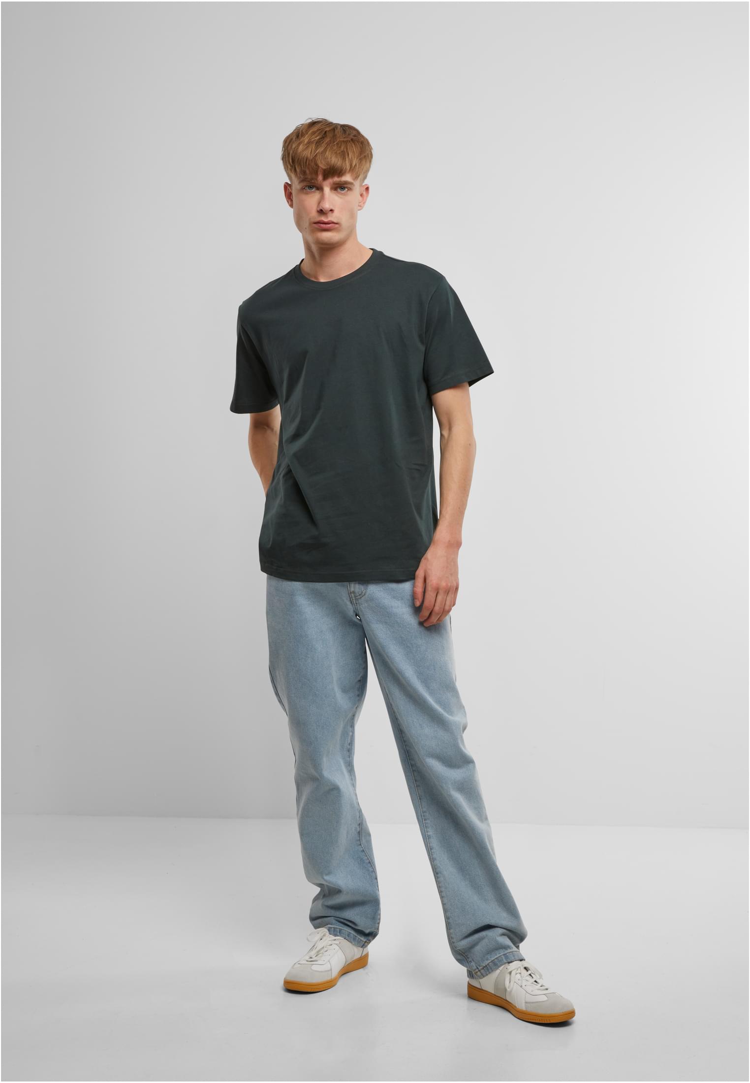 En manlig modell bär en mörkgrön B Premium Shirt med ljusblå jeans och vita sneakers.