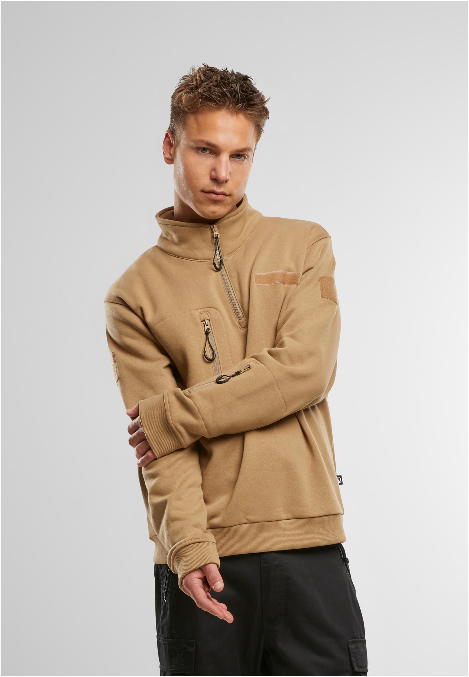 En man poserar framifrån och visar en beige B Tactical Sweat Troyer med hög krage och dragkedja.