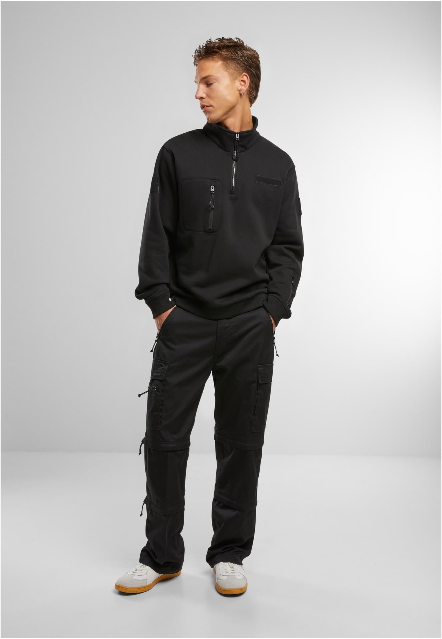 Helbild på en man som bär den svarta B Tactical Sweat Troyer-tröjan med svarta cargobyxor och vita sneakers.